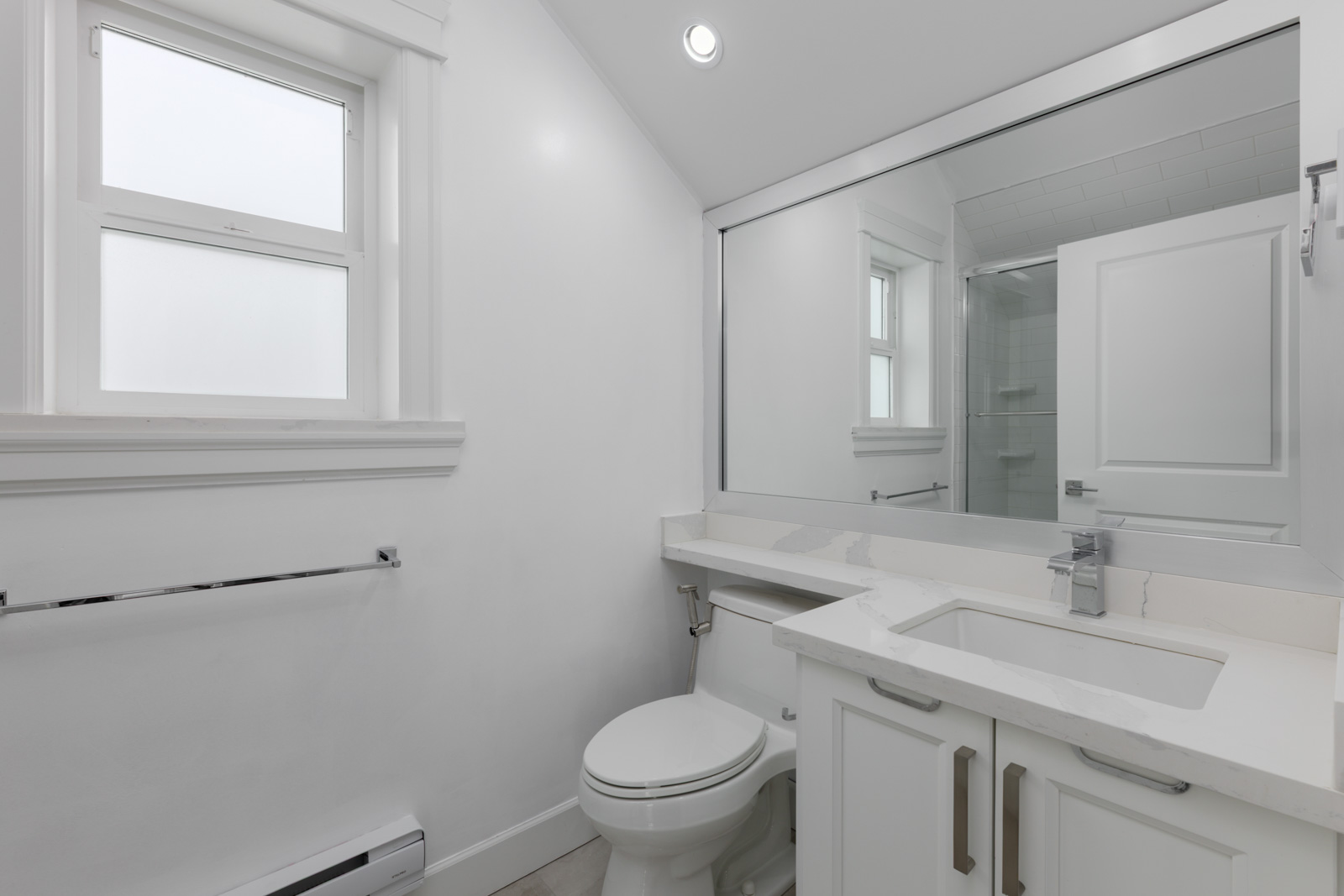Modern white bathroom on Falaise Ave, Vancouver, with sink, toilet, large mirror, towel bar, window, and minimal decor.