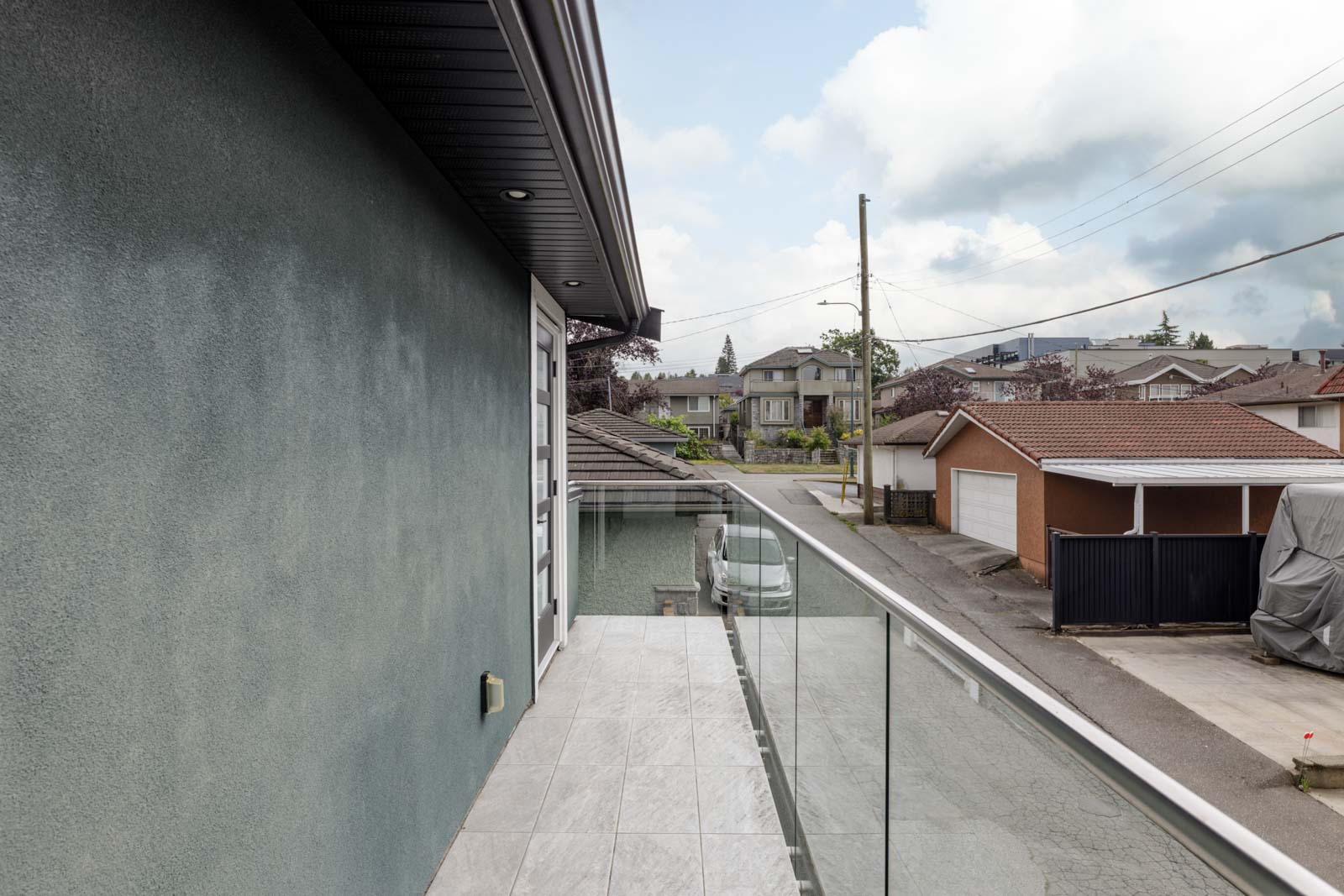 Balcony view with glass railing overlooking Vancouver’s Falaise Ave and Place, with houses, garages, and a covered car below.