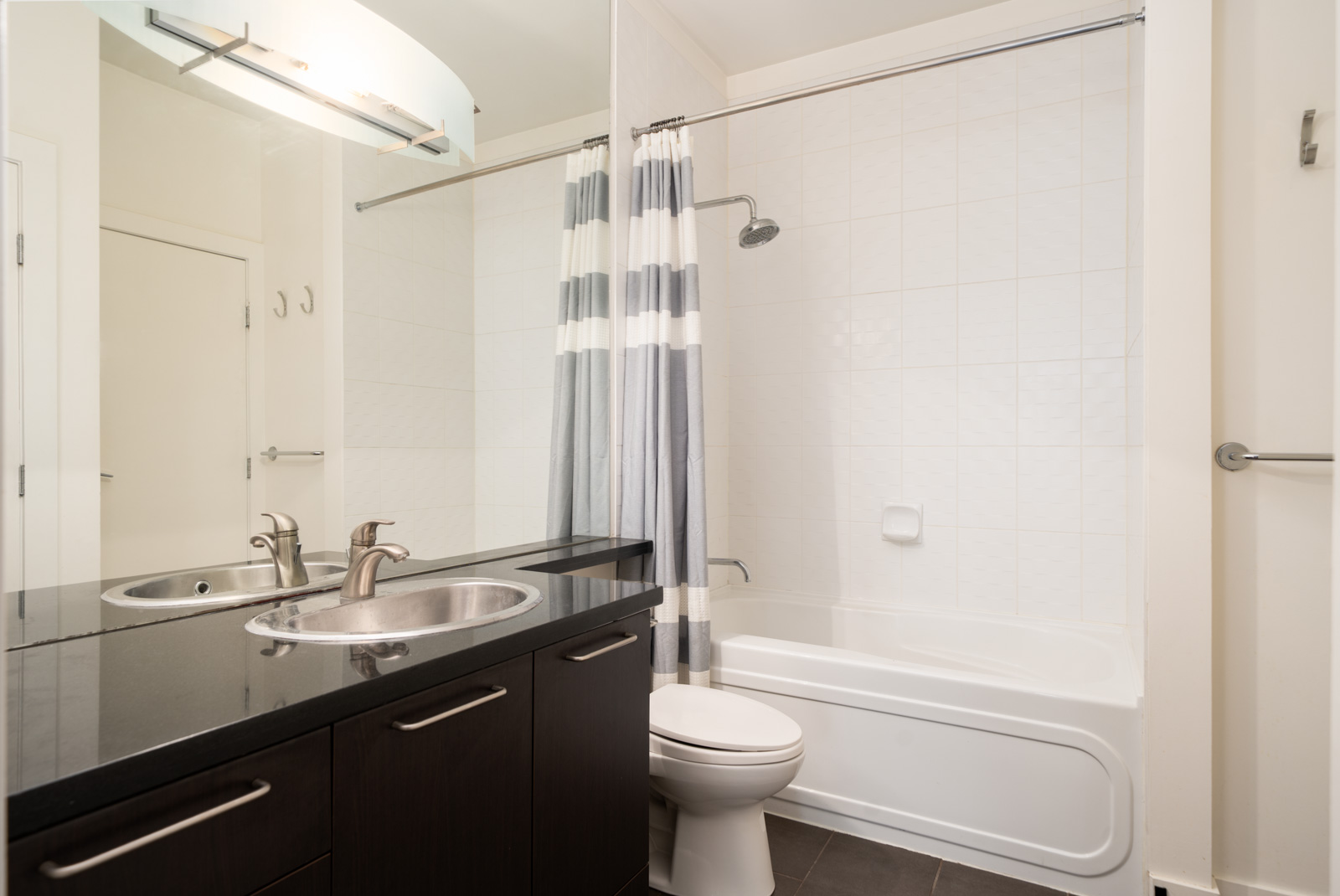 Modern bathroom at 205 E 10th Ave, Vancouver with double sink vanity, black countertop, toilet, and striped shower curtain.