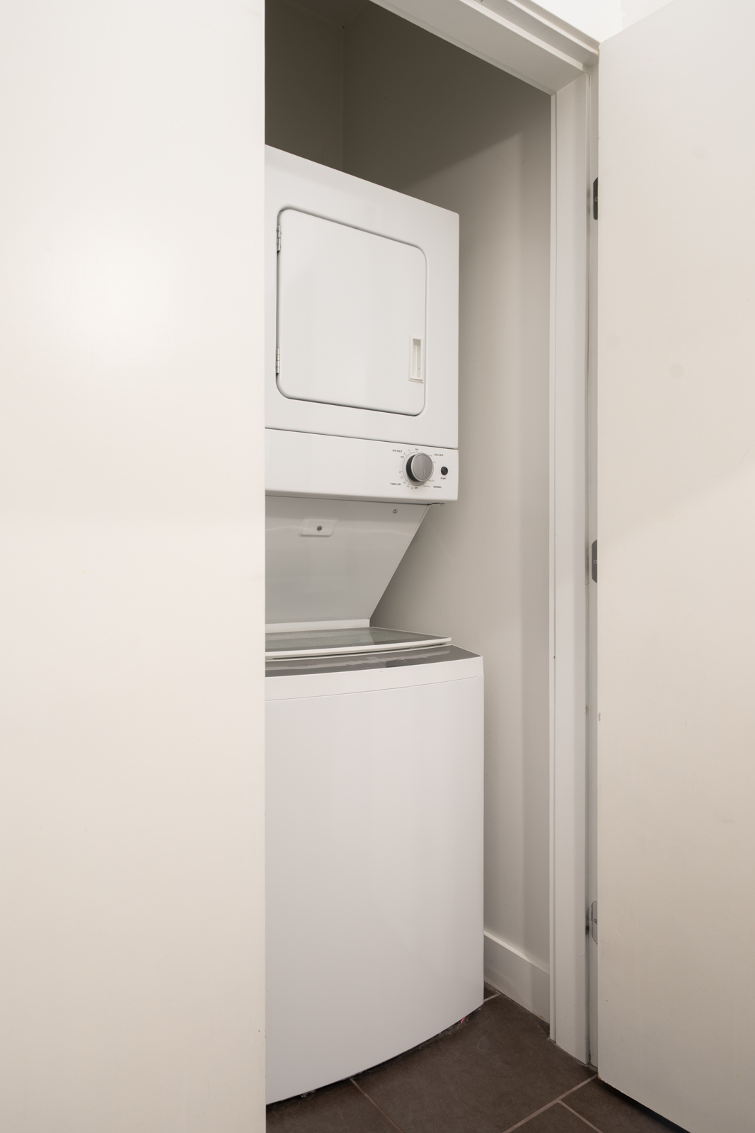 A white stacked washer and dryer sit in a small laundry closet with a partially open door in this 4th Floor Vancouver unit.