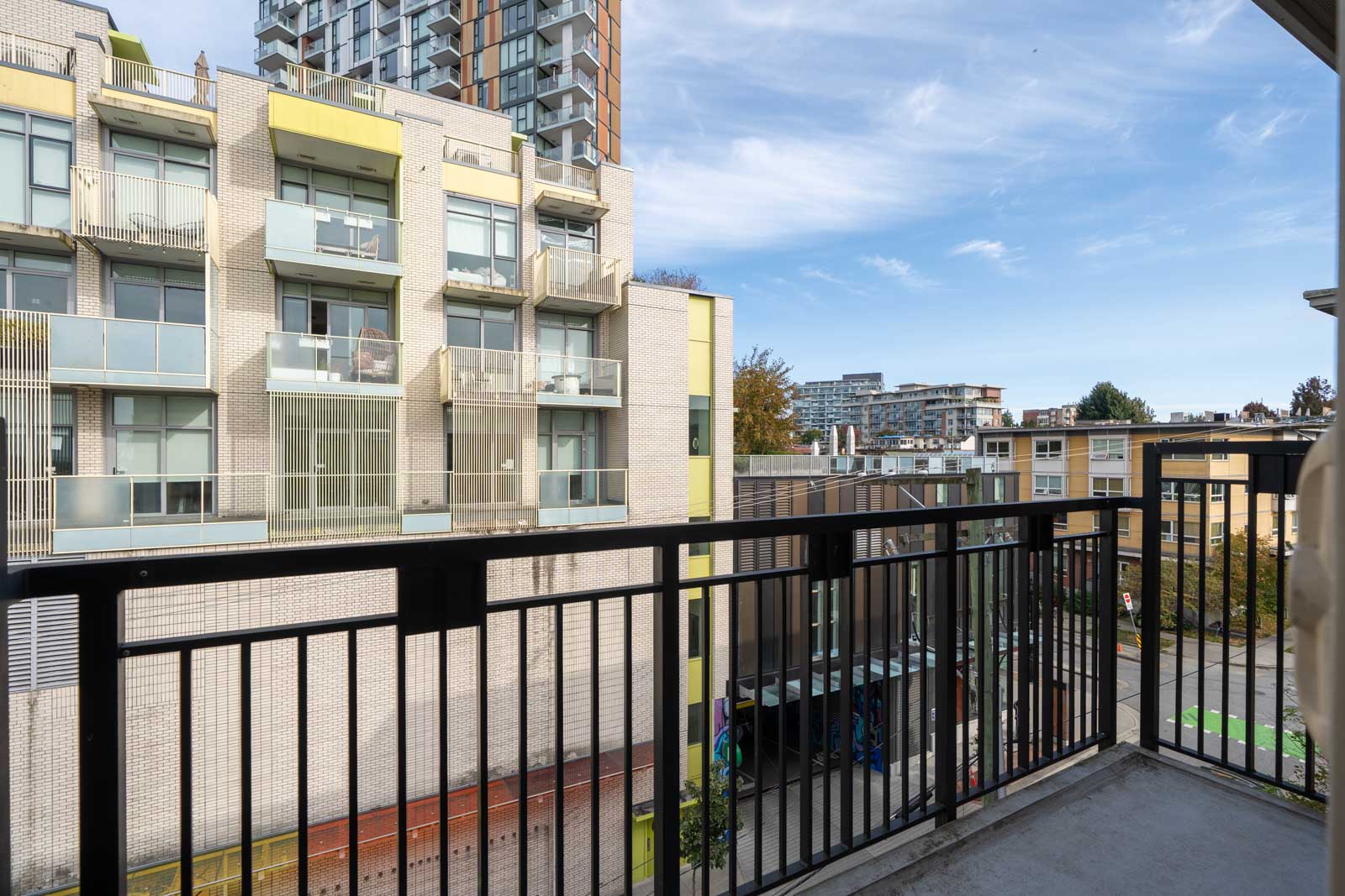 View from a 4th floor balcony with a black metal railing at 205 E 10th Ave, Vancouver, showing apartments and blue sky.