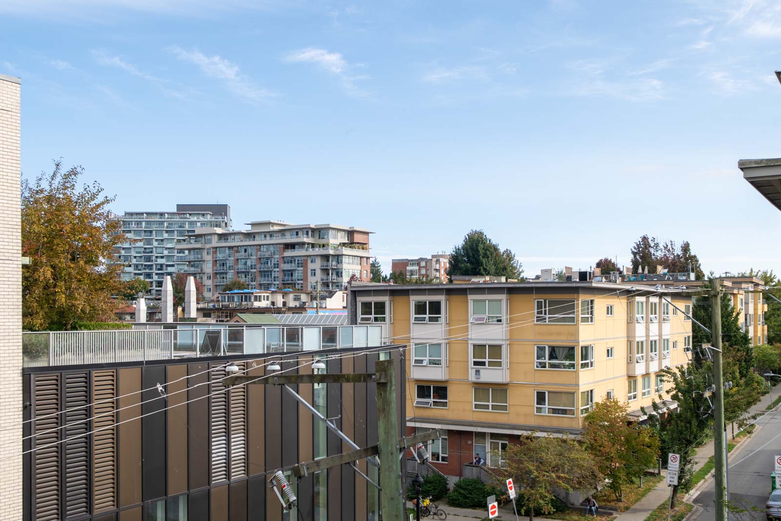 Residential and apartment buildings with trees, power lines, and street signs in the foreground near 205 E 10th Ave, Vancouver.