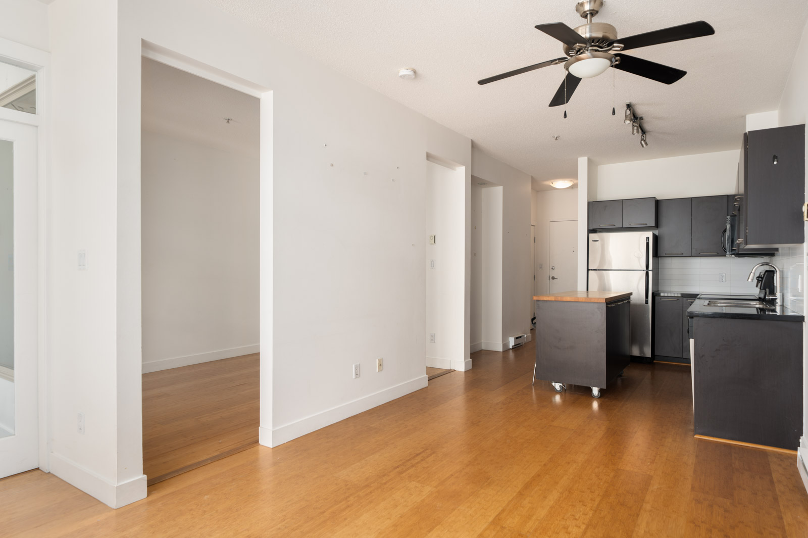 Apartment interior on 4th floor at 205 E 10th Ave, Vancouver with bamboo floors, white walls, ceiling fan, modern kitchen, and side room.