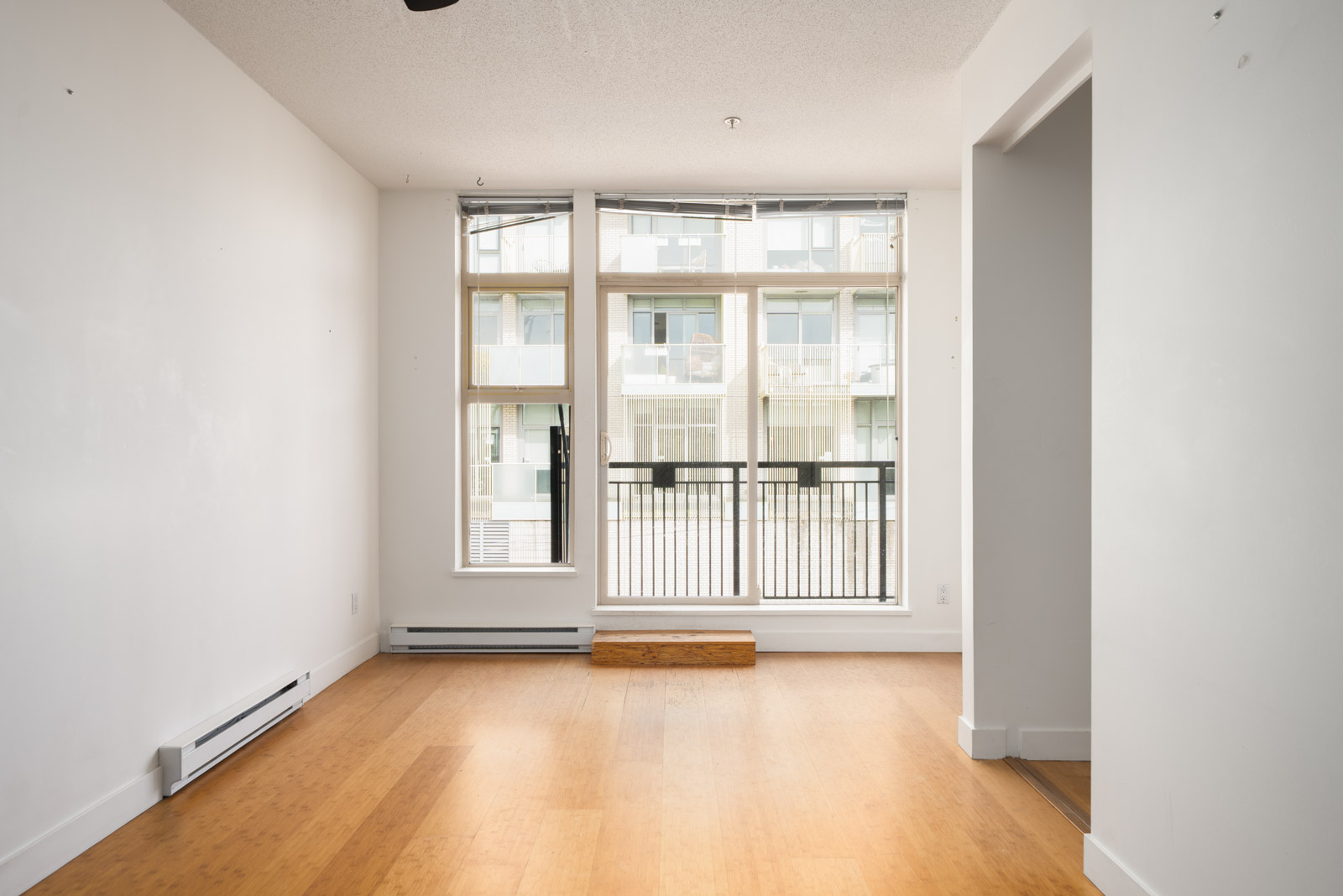 Empty room with white walls, light wood flooring, large windows, and a balcony railing visible; 4th floor, 205 E 10th Ave Vancouver.
