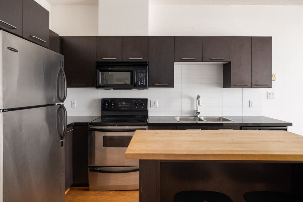 Modern kitchen on 4th floor, 205 E 10th Ave, Vancouver with dark cabinets, stainless appliances, and light wood island counter.