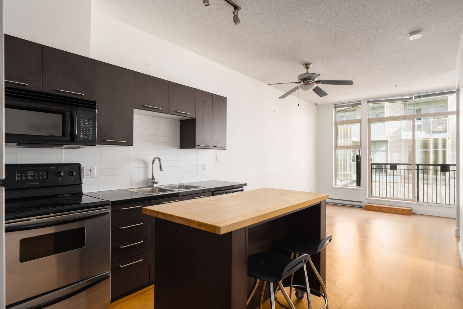 Modern kitchen at 205 E 10th Ave, Vancouver with dark cabinets, stainless appliances, wood island, two stools, and large windows.