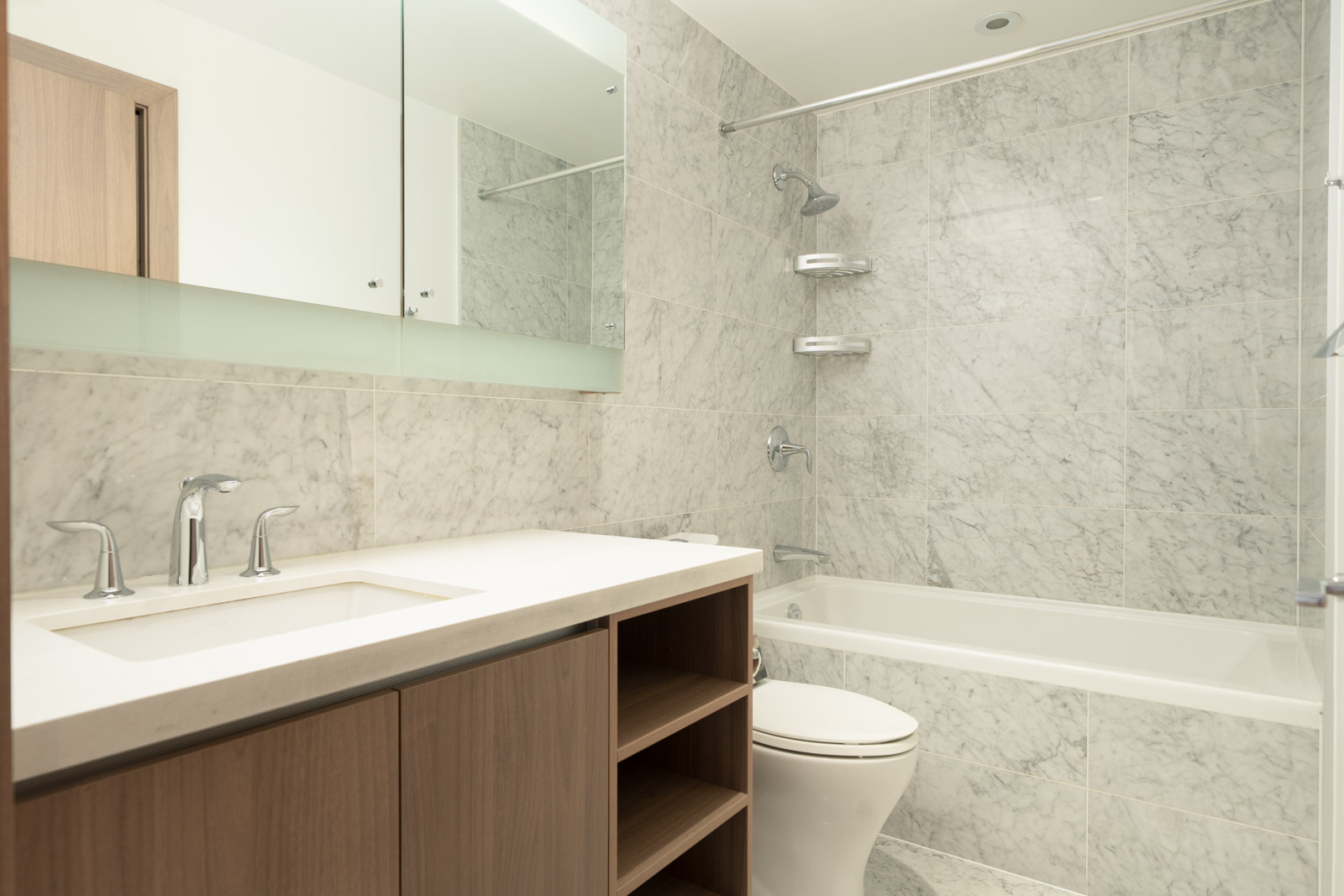 Modern bathroom in Burnaby at 6538 Nelson Ave with marble-tiled wall, tub-shower, built-in shelves, mirror, and wood vanity.
