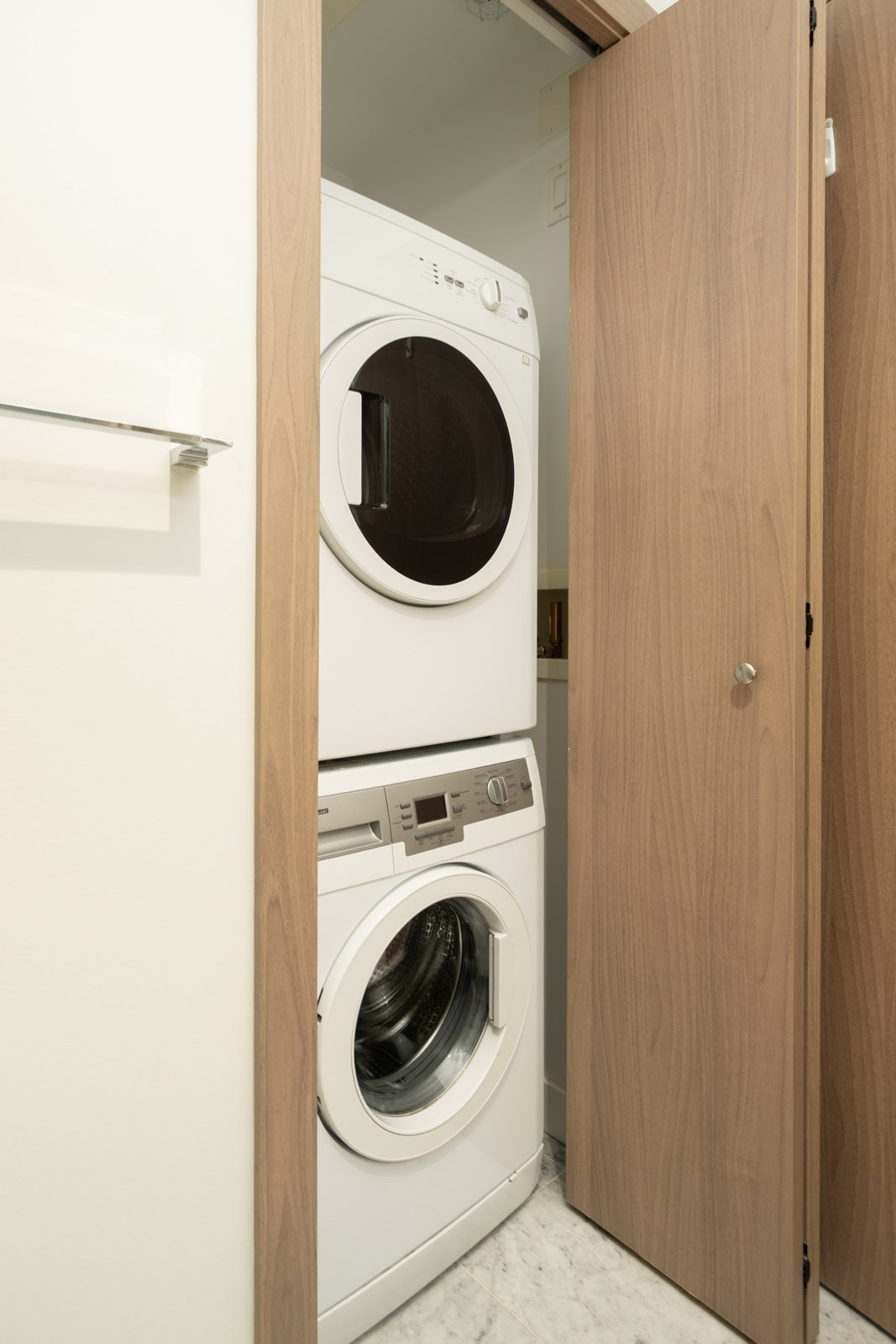 Stacked washer and dryer in a small closet with wooden doors, marble floor, on the 27th floor at 6538 Nelson Ave, Burnaby.