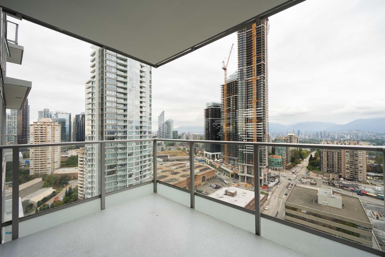 View from a high-rise balcony on Nelson Ave, showing Burnaby skyscrapers, construction areas, and busy streets under cloudy skies.