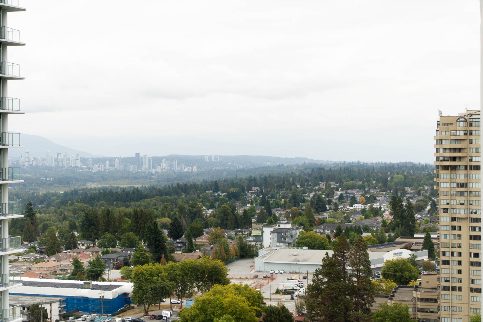 View from the 27th floor over Nelson Ave, Burnaby, showing residential and commercial buildings, trees, and distant high-rises.