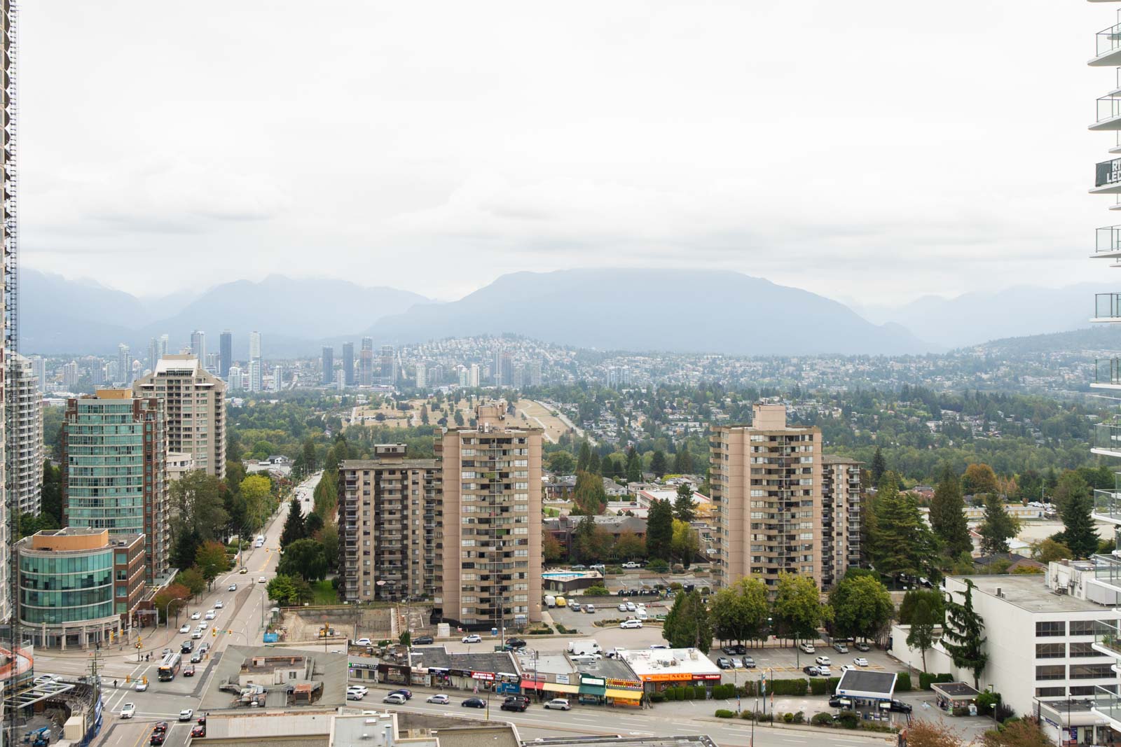 High-rise apartments on Nelson Ave, Burnaby, with mountains and other skyscrapers in the background beneath an overcast sky.