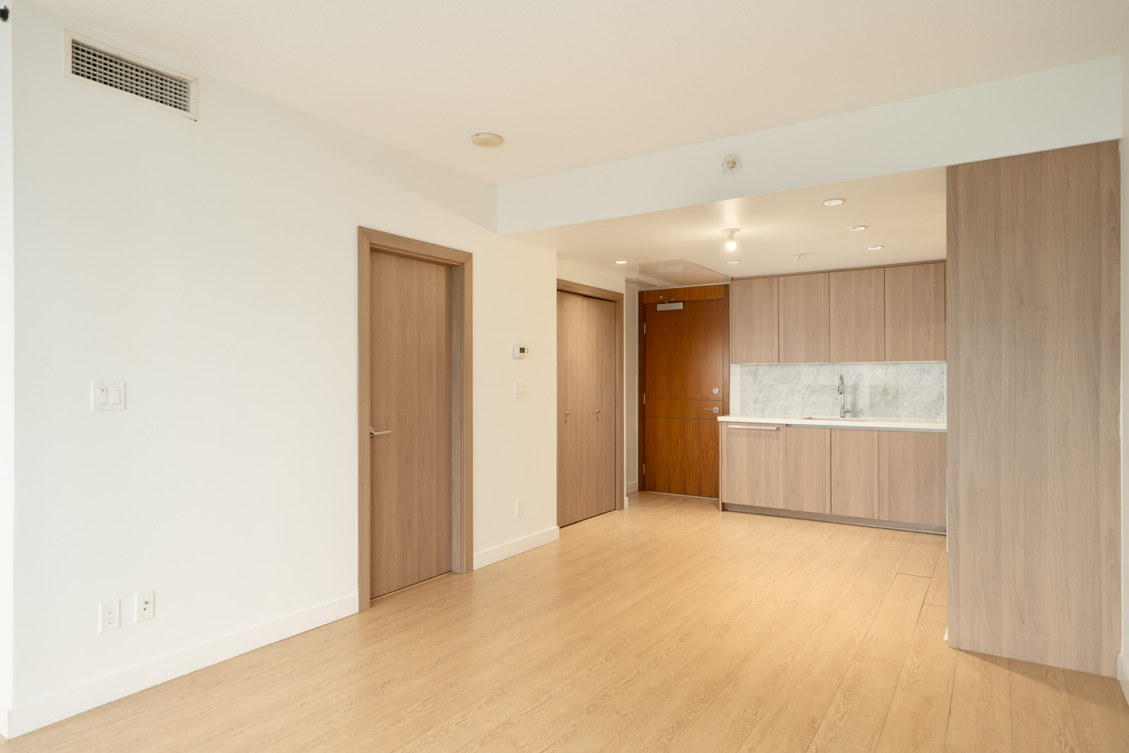 Unfurnished apartment at 6538 Nelson Ave, Burnaby, with light wood floors, two doors, white walls, and a kitchenette.