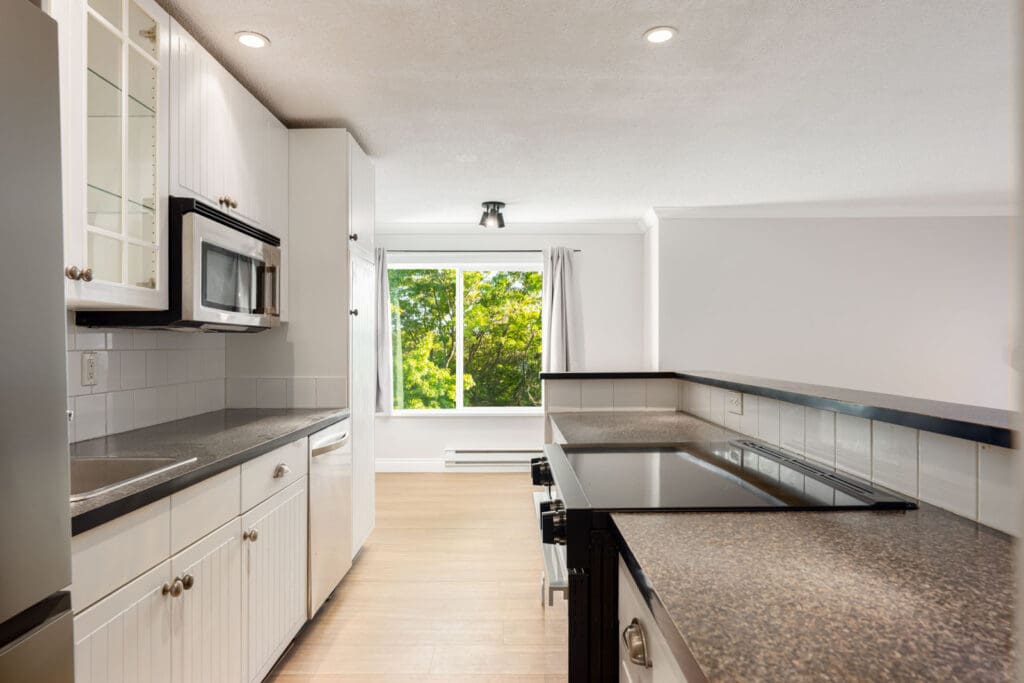 Modern 3rd floor Richmond kitchen with white cabinets, black countertops, electric stove, built-in microwave, and large window.