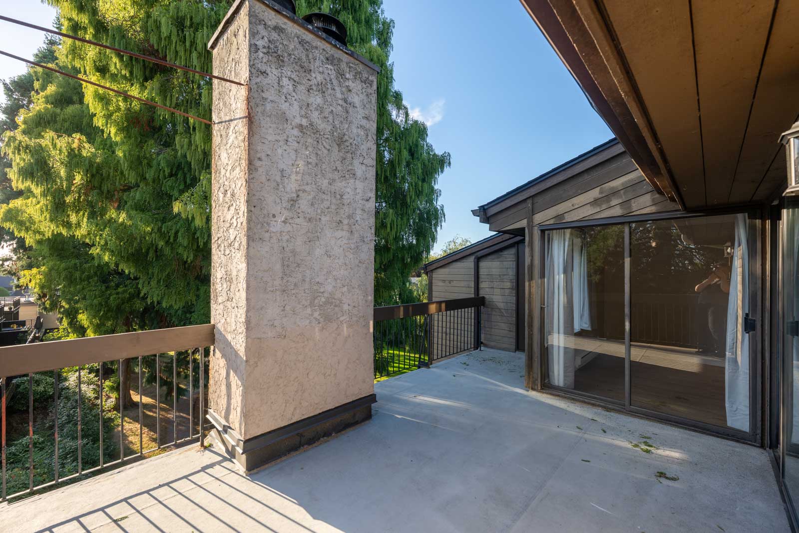 Second-floor concrete balcony with metal railing and chimney, next to sliding glass doors, under a clear Richmond sky.