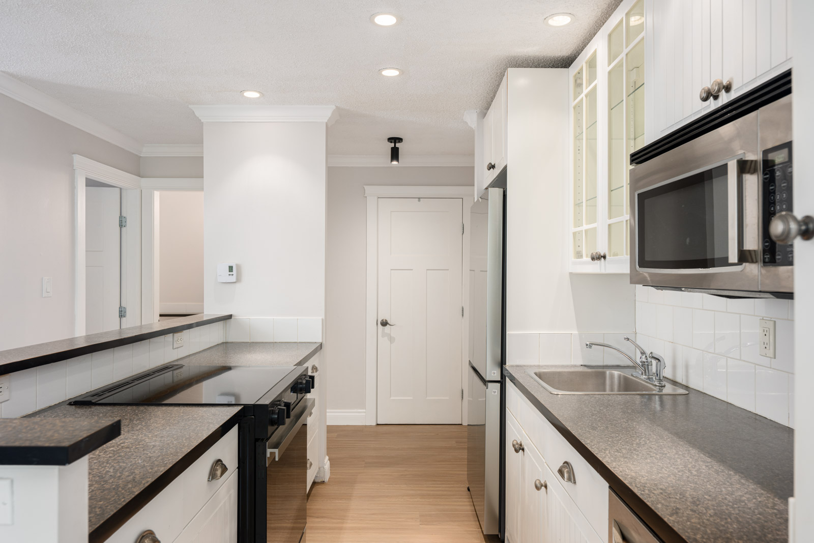 Modern kitchen with white cabinets, black counters, stove, sink, microwave, tiled backsplash, wood floor; Richmond 3rd floor.