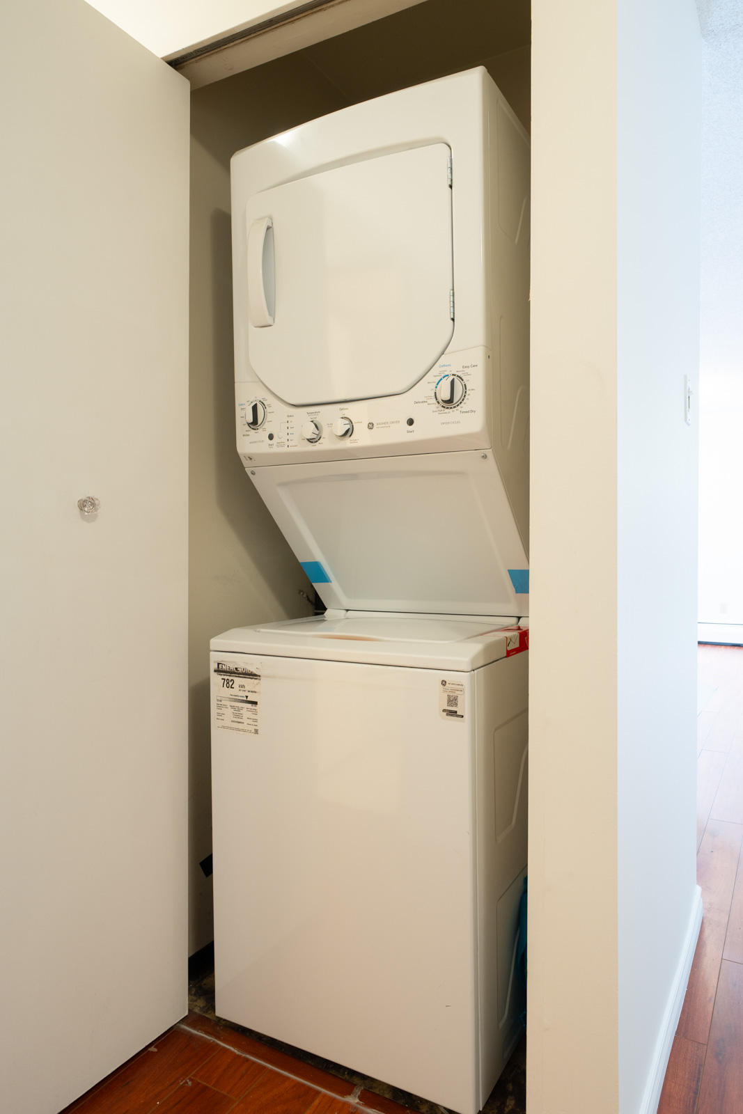 Stacked washer and dryer in a small laundry closet with an open door on hardwood floor at 8460 Ackroyd Rd, Richmond, first floor.