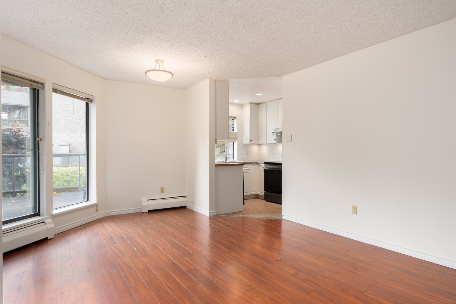 Unfurnished room at 8460 Ackroyd Rd, Richmond, with wood floors, white walls, two large windows, and open kitchen.