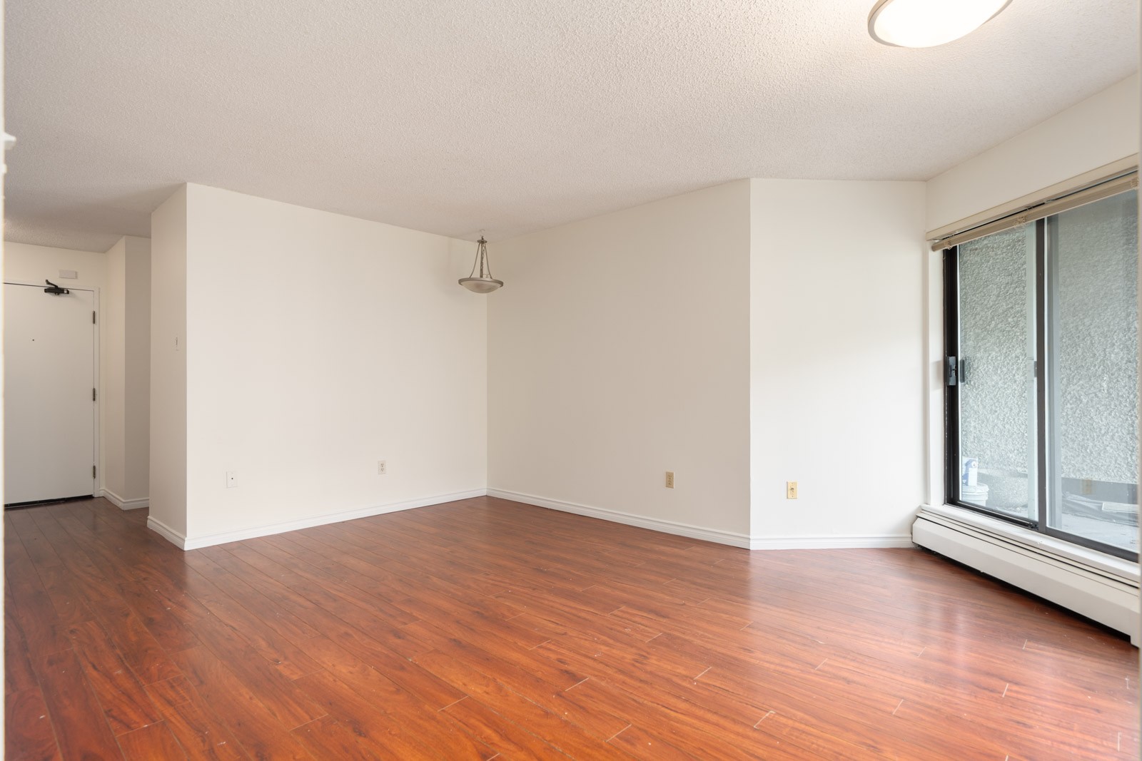 Empty 1st floor room with white walls, wood-style flooring, ceiling light, and large sliding doors to a balcony in Richmond.