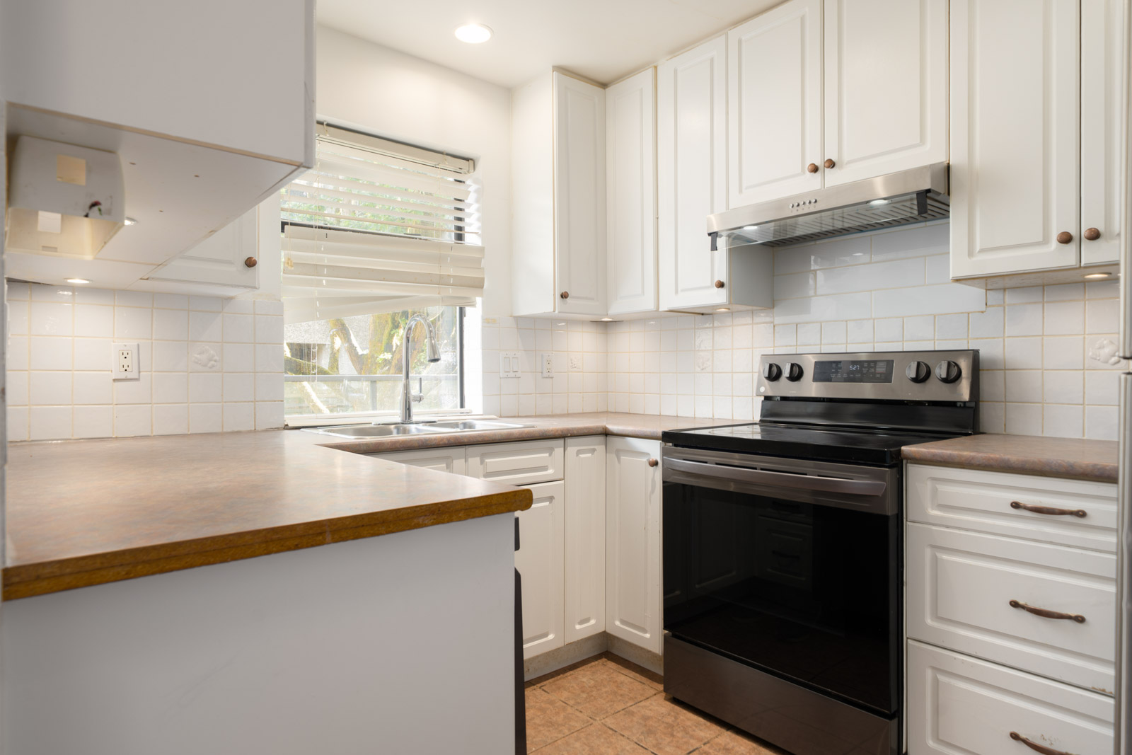 Small kitchen in Richmond with white cabinets, electric stove, range hood, brown counters, tiled backsplash, and window blinds.
