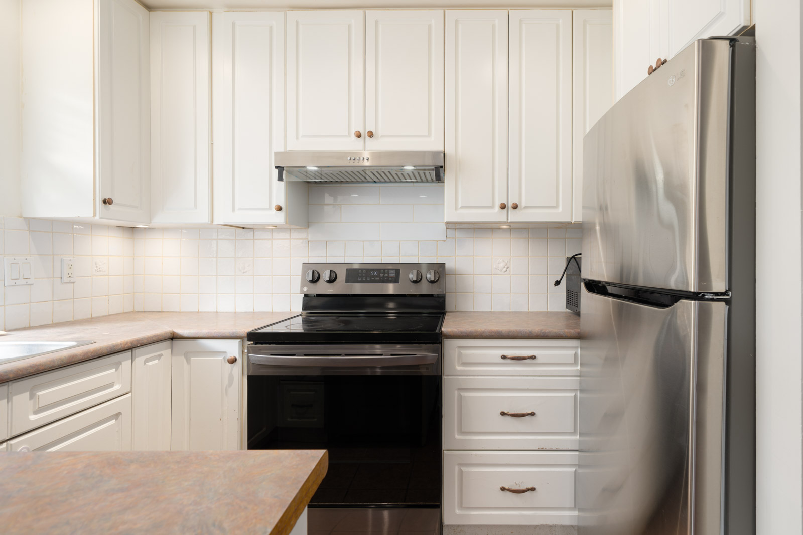 Modern kitchen on the 1st floor at 8460 Ackroyd Rd, Richmond with white cabinets, stainless fridge, and tiled backsplash.