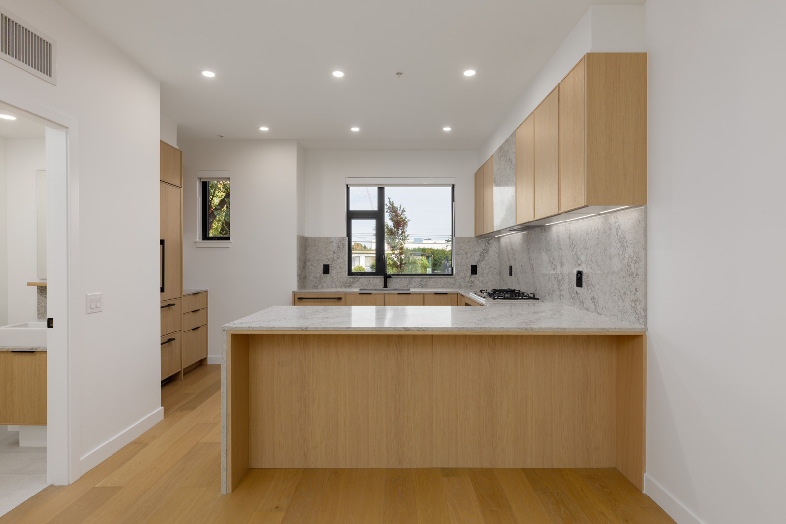 Modern kitchen at 5433 Oak Street featuring light wood cabinetry, white marble countertops, and a central peninsula.