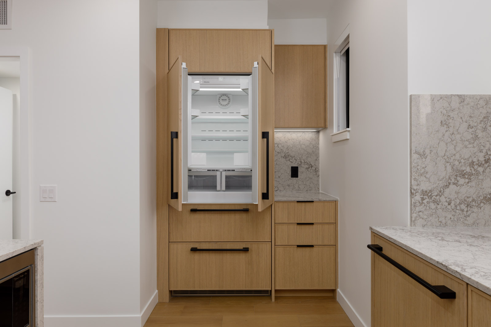 Light wood cabinets in a Vancouver townhouse kitchen, shown with the double doors of a built-in refrigerator open.
