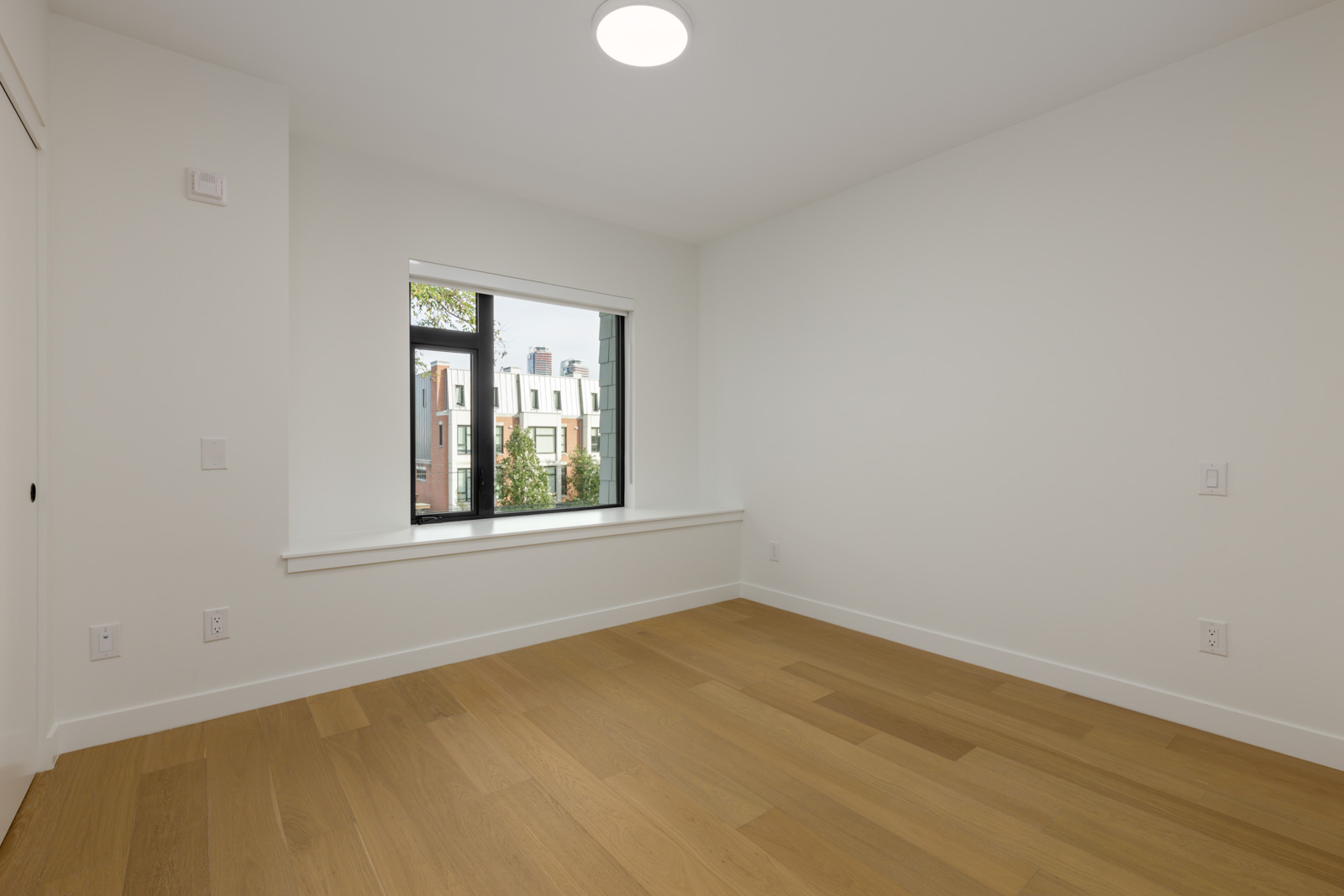 Empty room with white walls and wood floors, showing a view of brick buildings at the 5433 Oak Street townhouse.