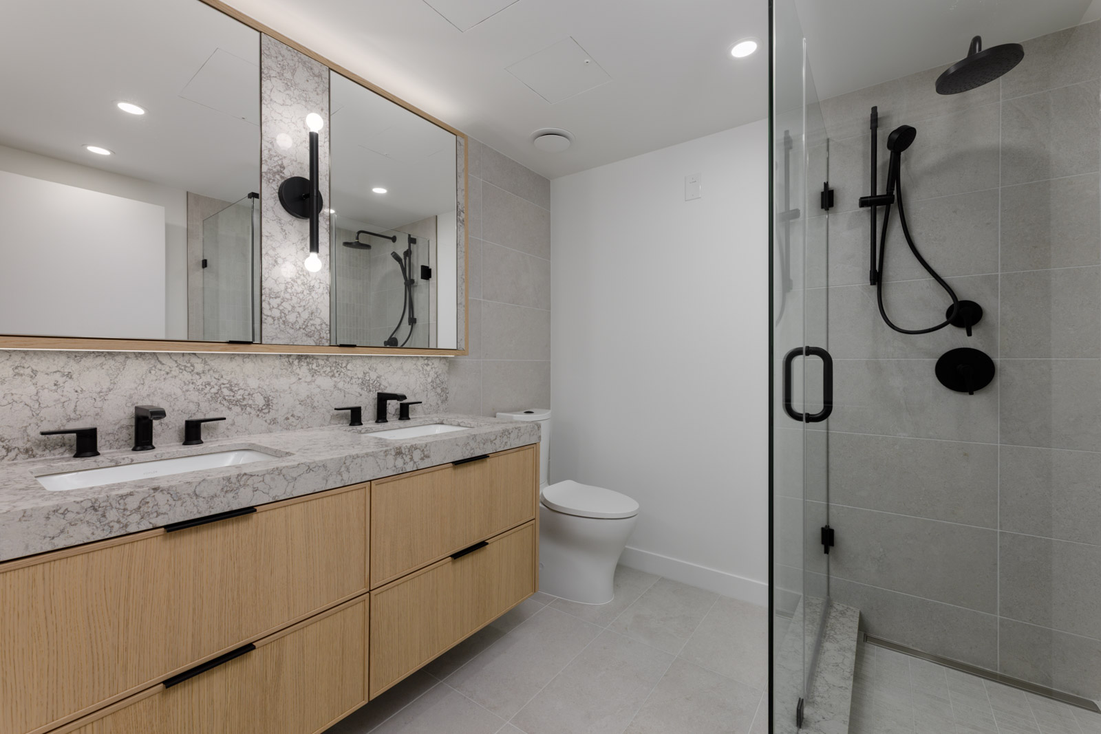 Modern bathroom at 5433 Oak Street with a double wood vanity, marble countertop, toilet, and glass-enclosed walk-in shower.