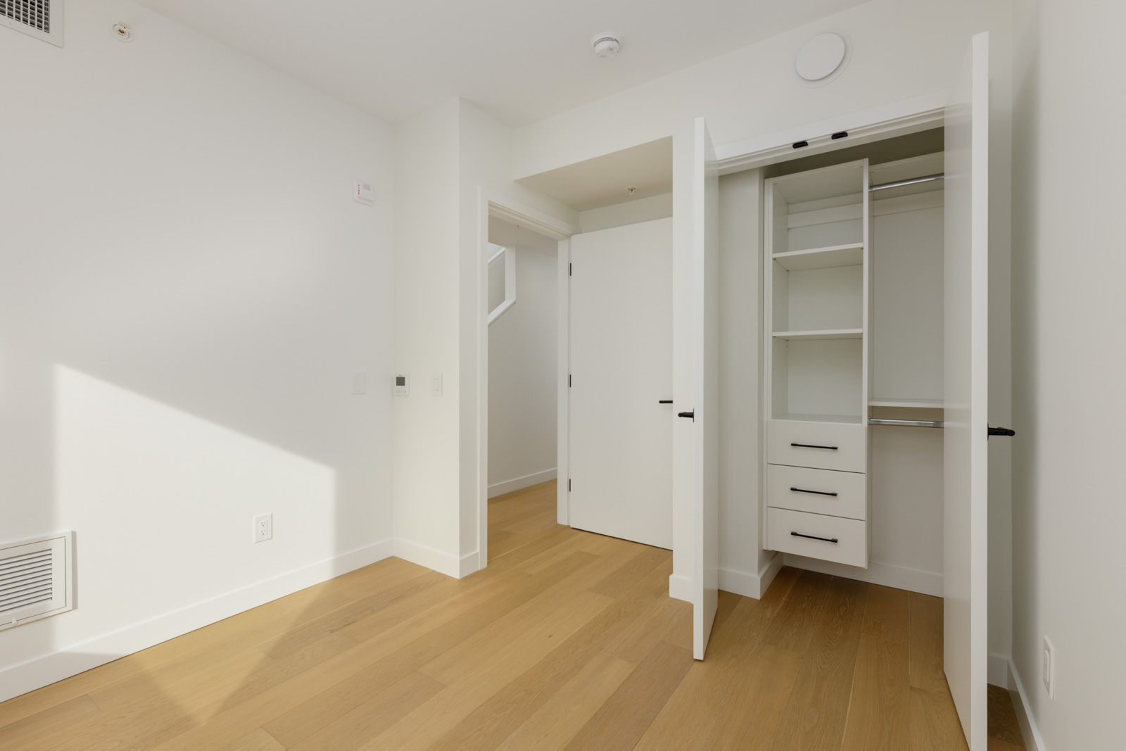 Empty room at 5433 Oak Street with hardwood floors, a doorway, and an open closet with built-in shelves and drawers.