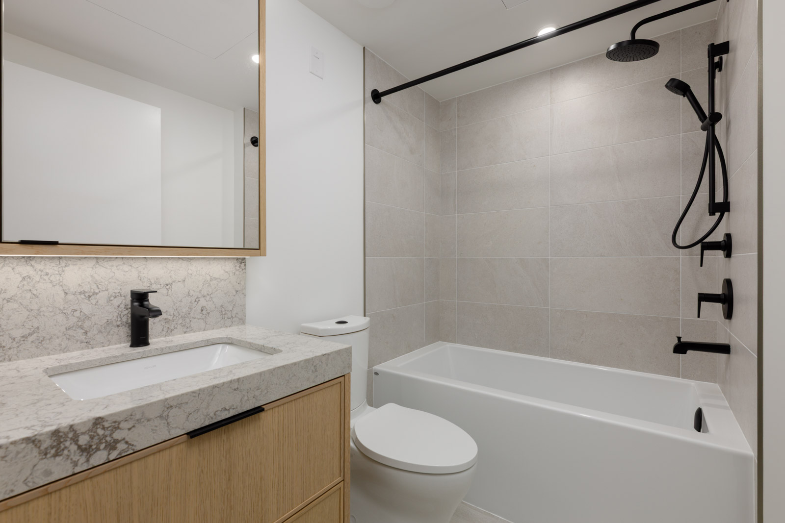Bathroom at 5433 Oak Street with a light wood vanity, stone counter, toilet, and bathtub with a black shower fixture.