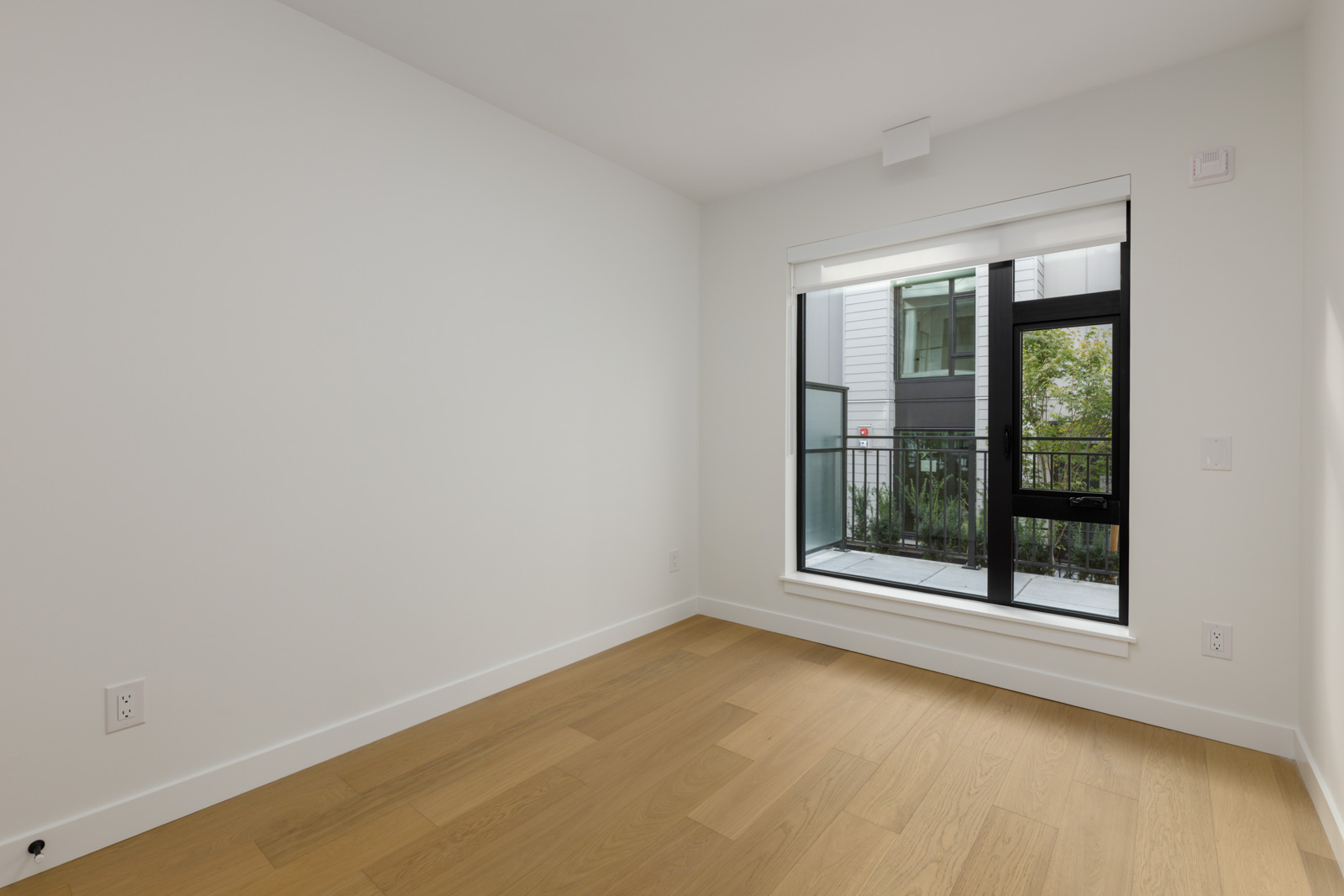 Empty room with white walls, wood floors, and a balcony glass door in a 5433 Oak Street, Vancouver townhouse.