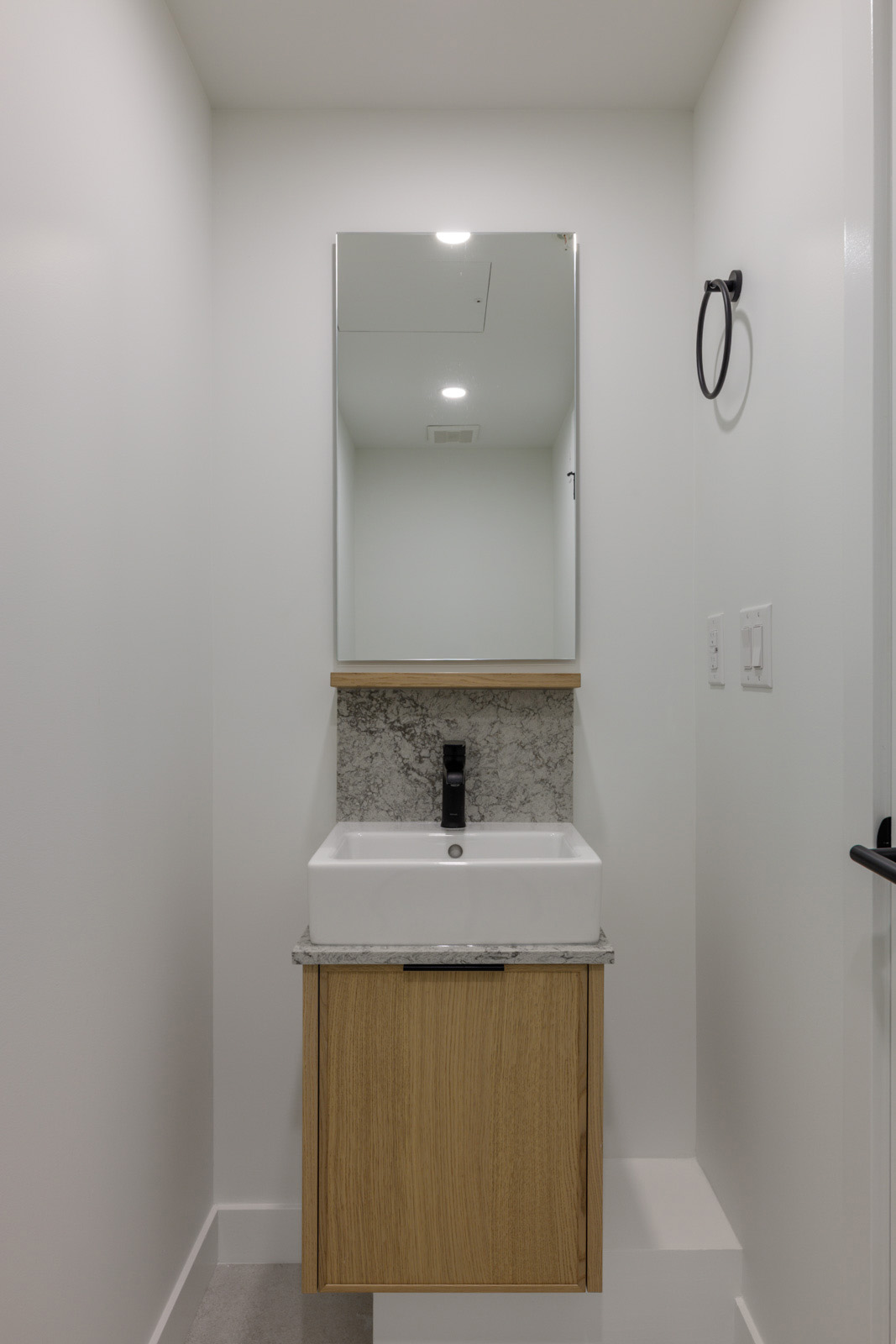 Wall-mounted vanity with a white vessel sink, black faucet, and rectangular mirror in a Vancouver townhouse.