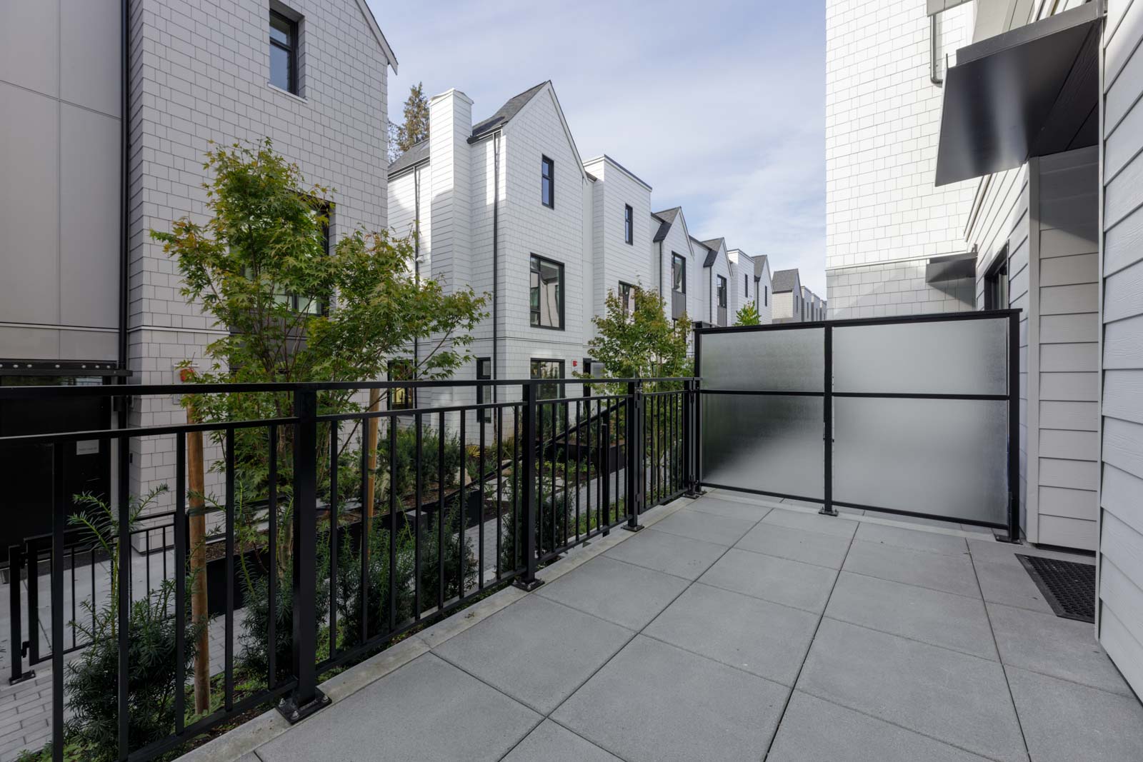 A paved balcony with a black metal railing overlooking a row of white Vancouver townhouses.