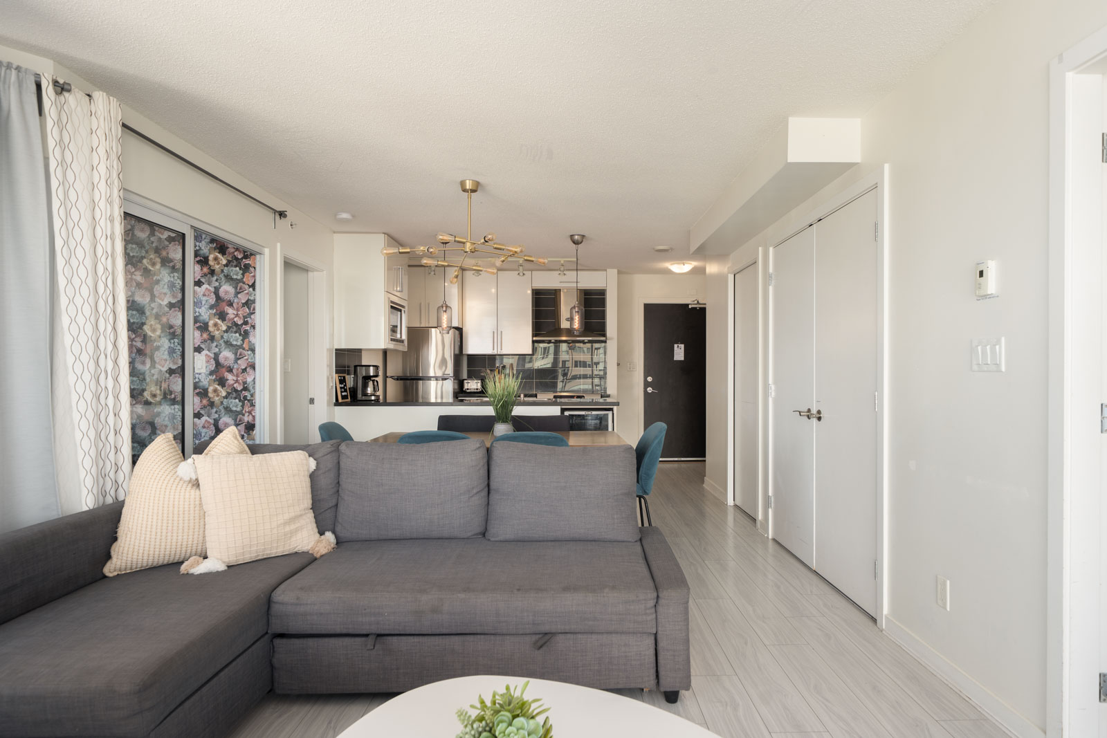 Grey sectional sofa in a living area facing an open kitchen and dining space with blue chairs at 689 Abbott St, Vancouver.