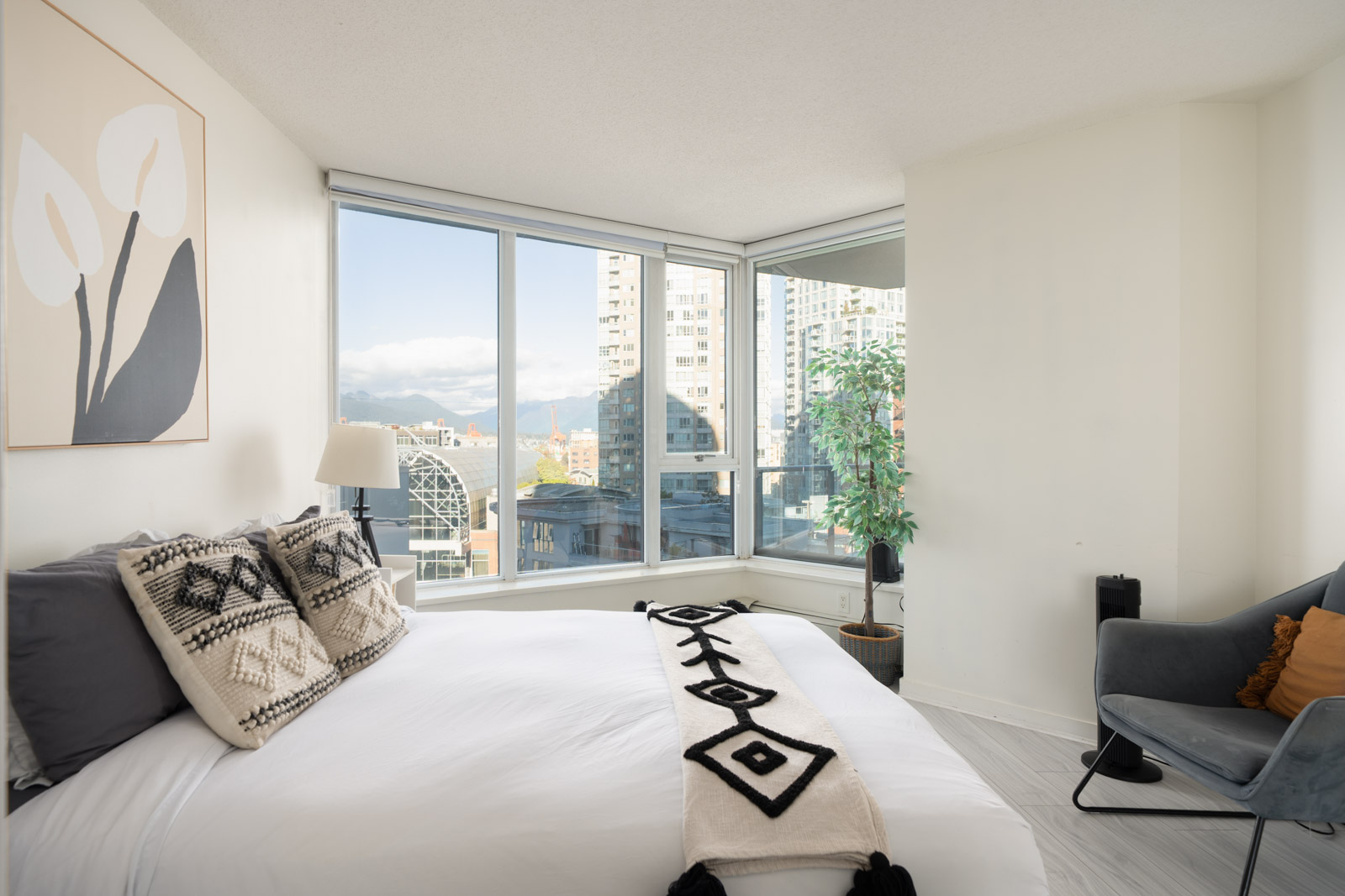 Bedroom with a bed, patterned pillows and runner, and an armchair overlooking the Vancouver skyline at 689 Abbott St.