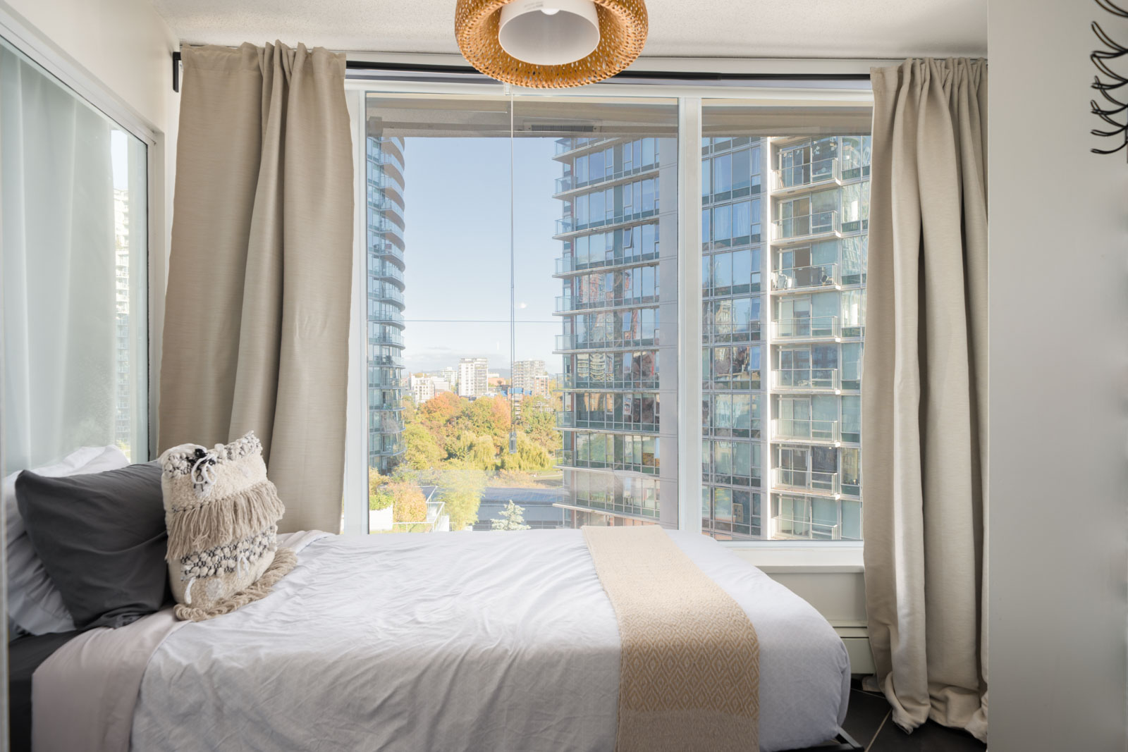 A bedroom at 689 Abbott St, Vancouver, with a large window overlooking high-rise buildings and a park.