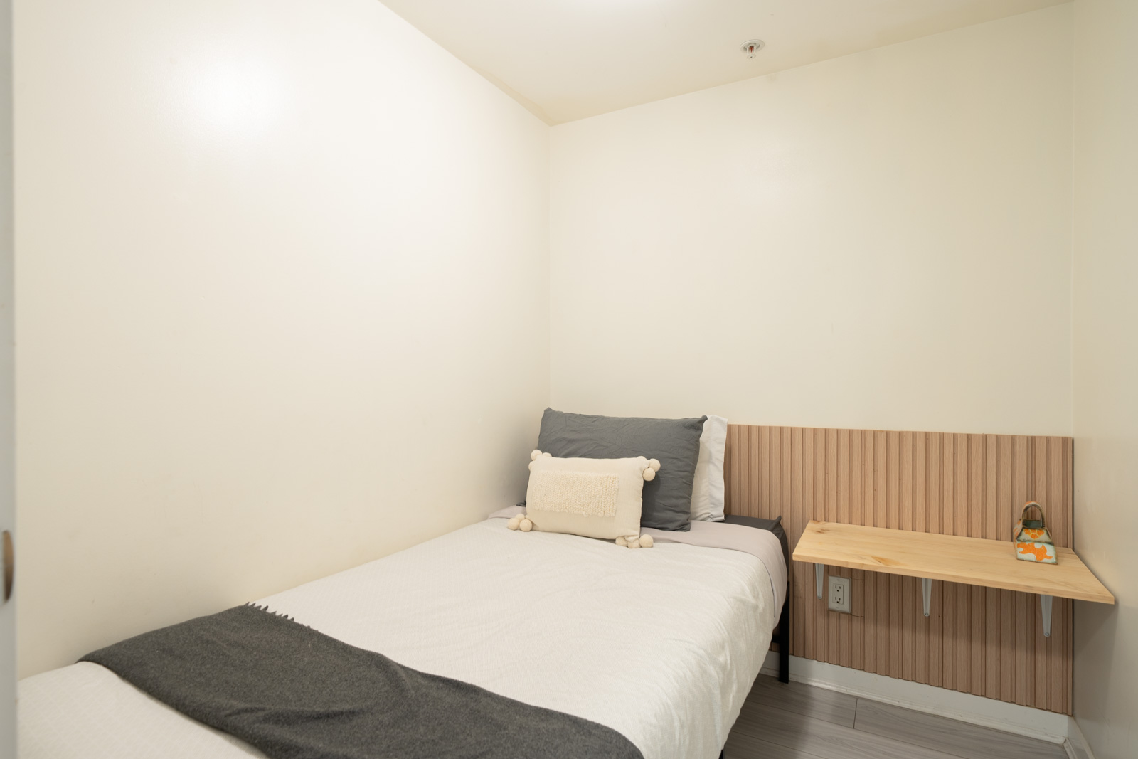 Single bed with grey and white bedding next to a wall-mounted wooden desk in a 689 Abbott St Vancouver condo.