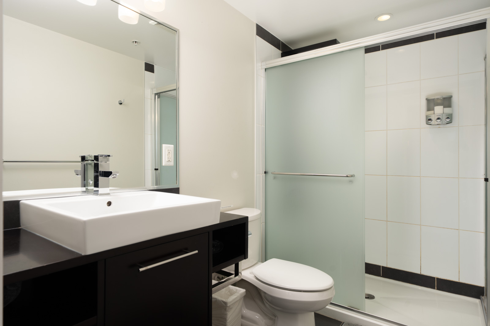 Bathroom at 689 Abbott Street, Vancouver, featuring a square white sink on a dark vanity, a toilet, and a glass shower.