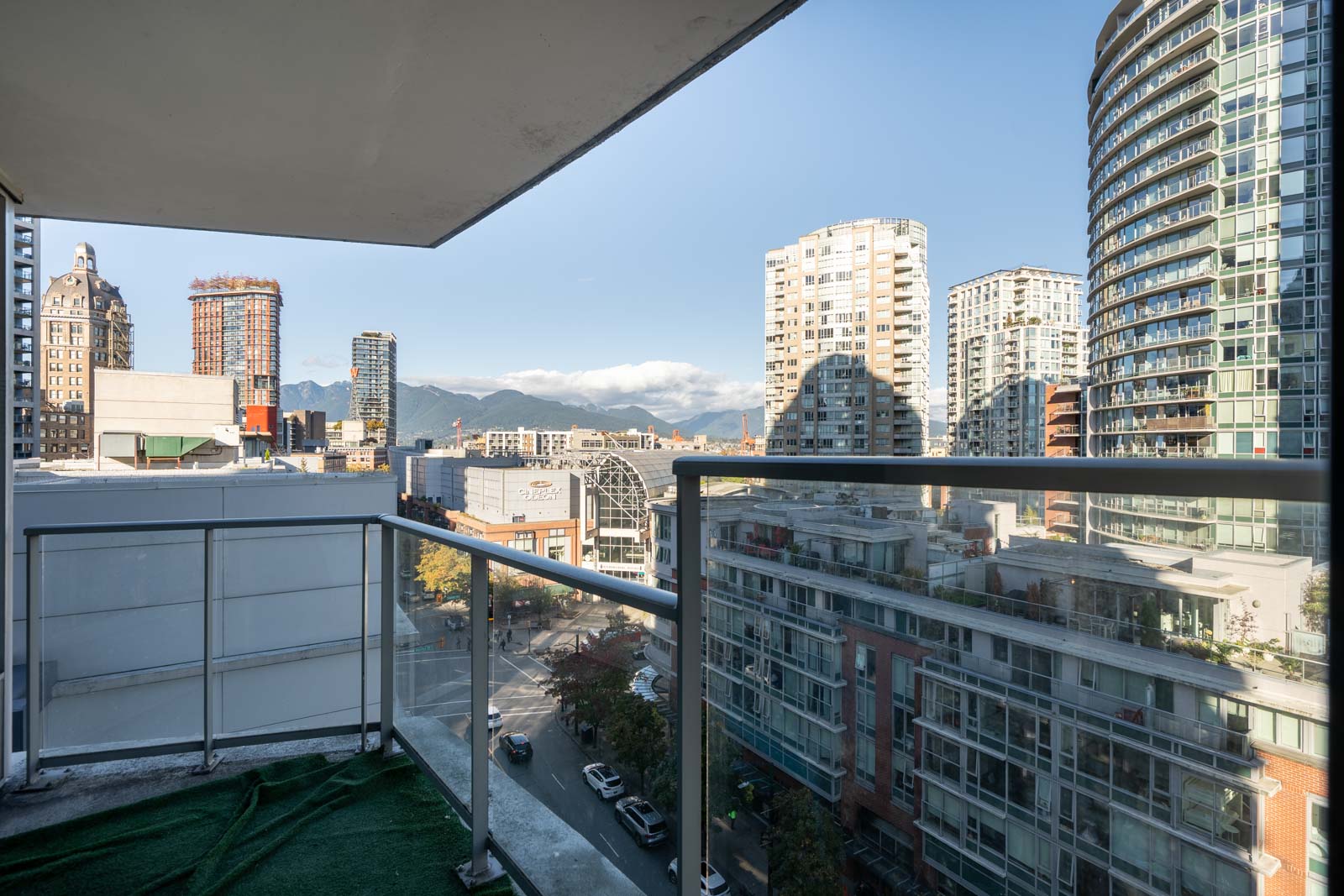 View from a high-rise balcony at 689 Abbott St, overlooking city streets and apartment towers toward distant mountains.