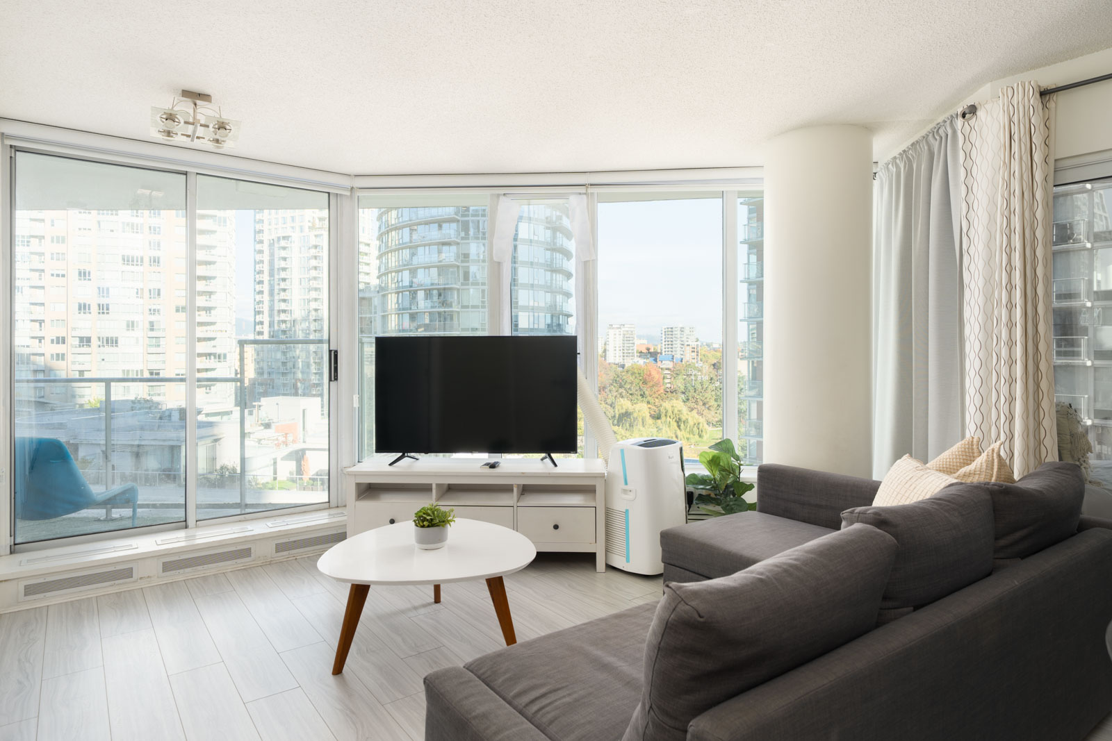 Grey sectional, TV on white console, and coffee table facing floor-to-ceiling windows in a 10th-floor apartment at 689 Abbott.