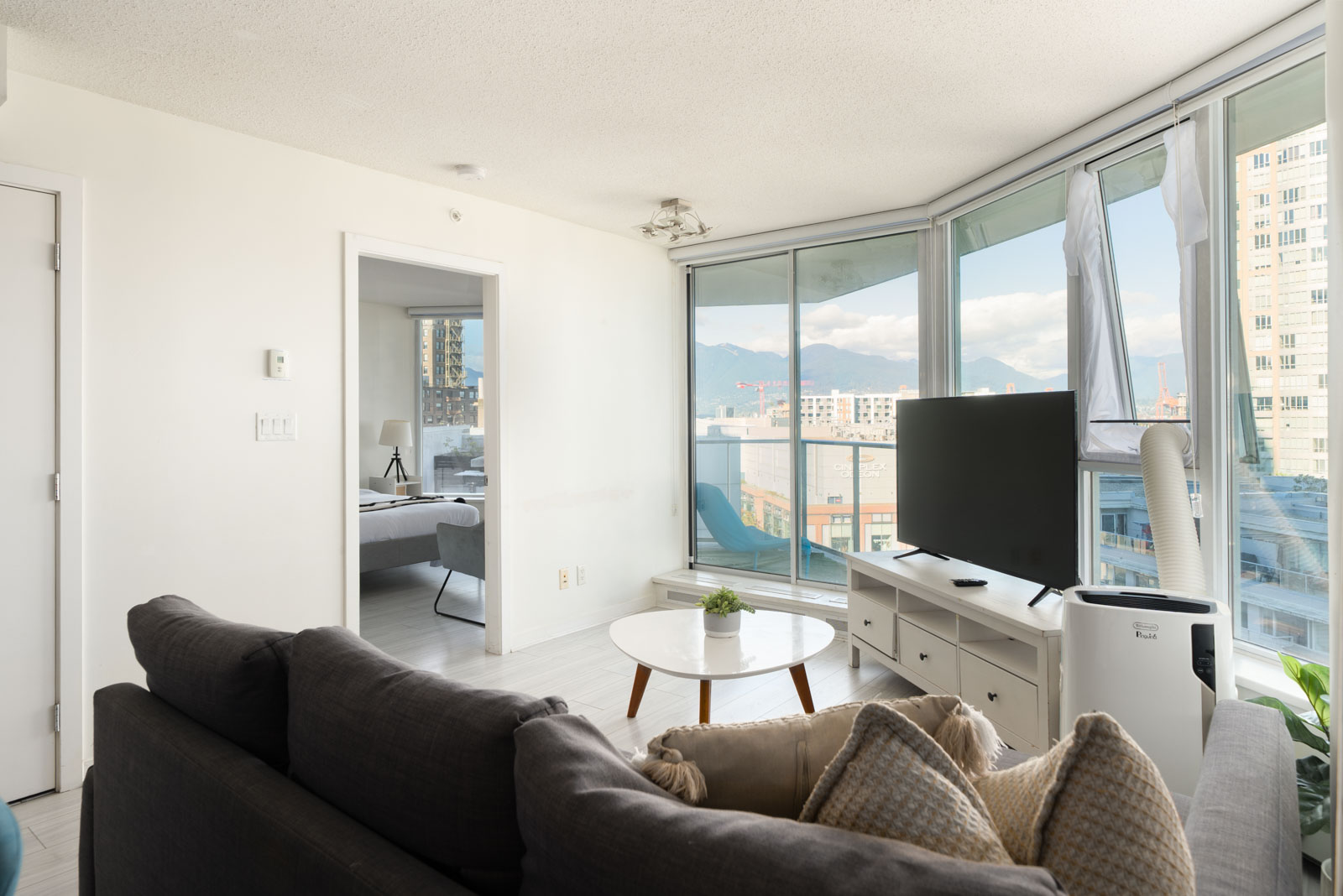 Living room at 689 Abbott St with a sofa, TV on a white console, and coffee table, overlooking Vancouver and mountains.