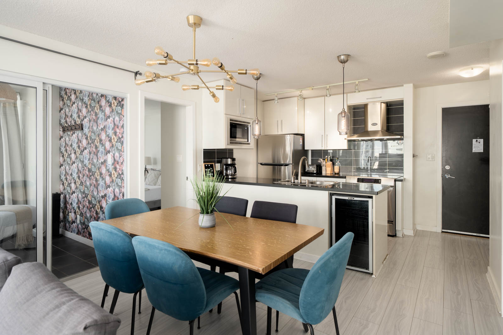 Dining area at 689 Abbott St featuring a wooden table, four blue upholstered chairs, and a plant, facing an open kitchen.