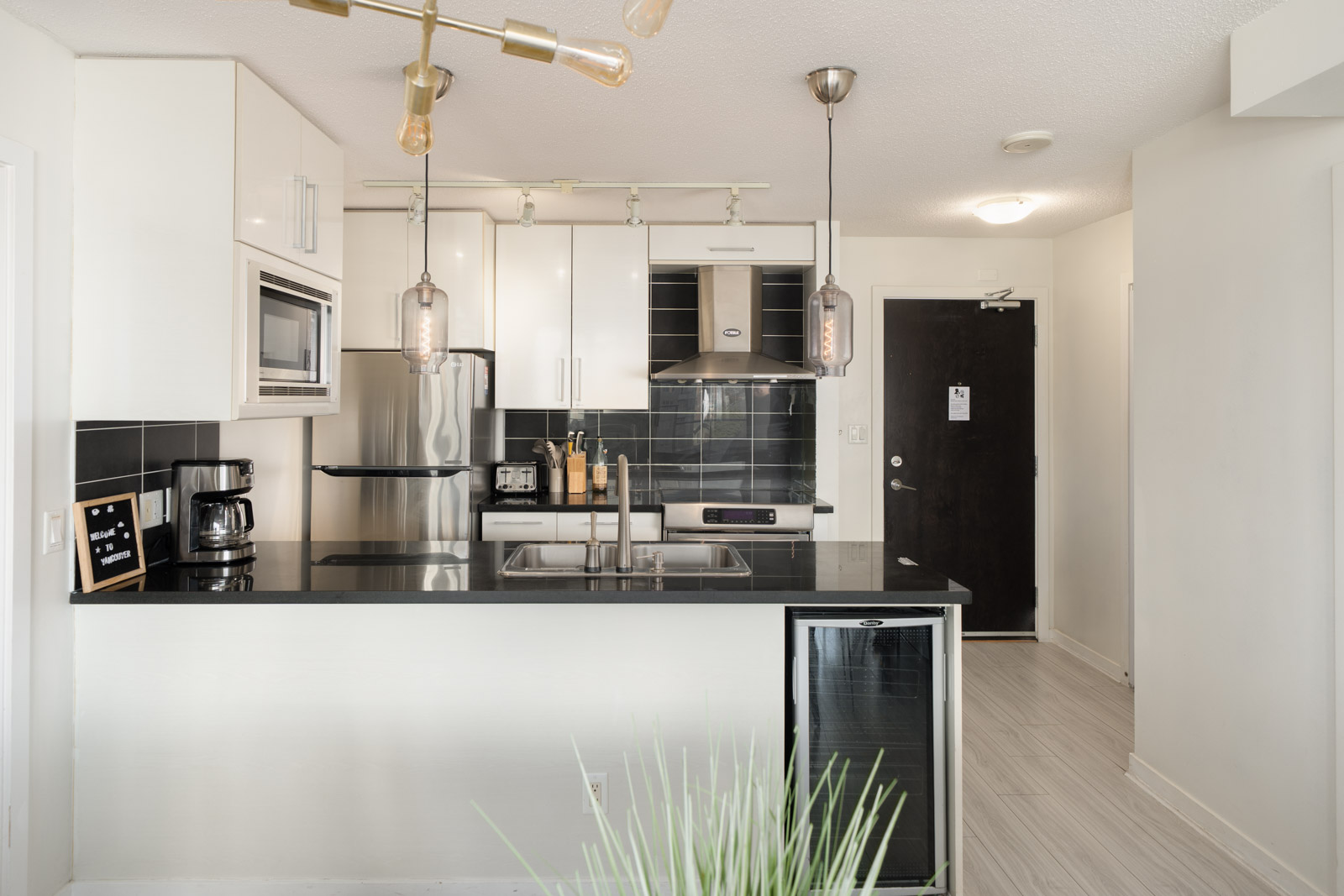 Modern kitchen at 689 Abbott St featuring white cabinets, black countertops, stainless steel appliances, and a beverage fridge.
