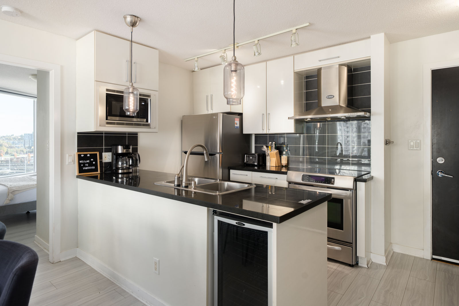 Kitchen at 689 Abbott Street with white cabinets, black countertops, stainless appliances, and “Welcome to Vancouver” sign.