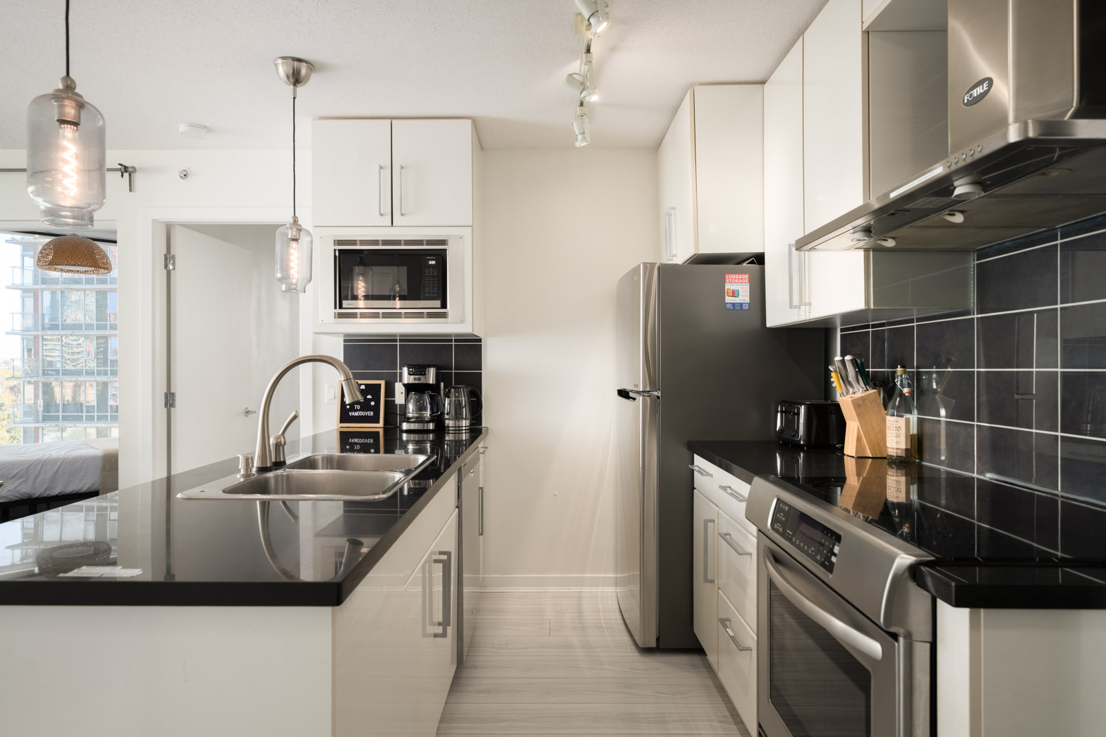 Modern 10th-floor Vancouver kitchen with white cabinetry, black countertops, stainless steel appliances, and a double-basin sink.