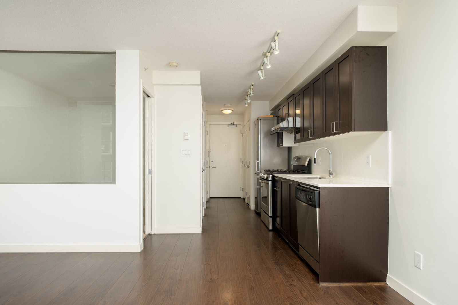 A narrow Vancouver kitchen with dark wood cabinets and stainless steel appliances, opening to a hallway with a white door.