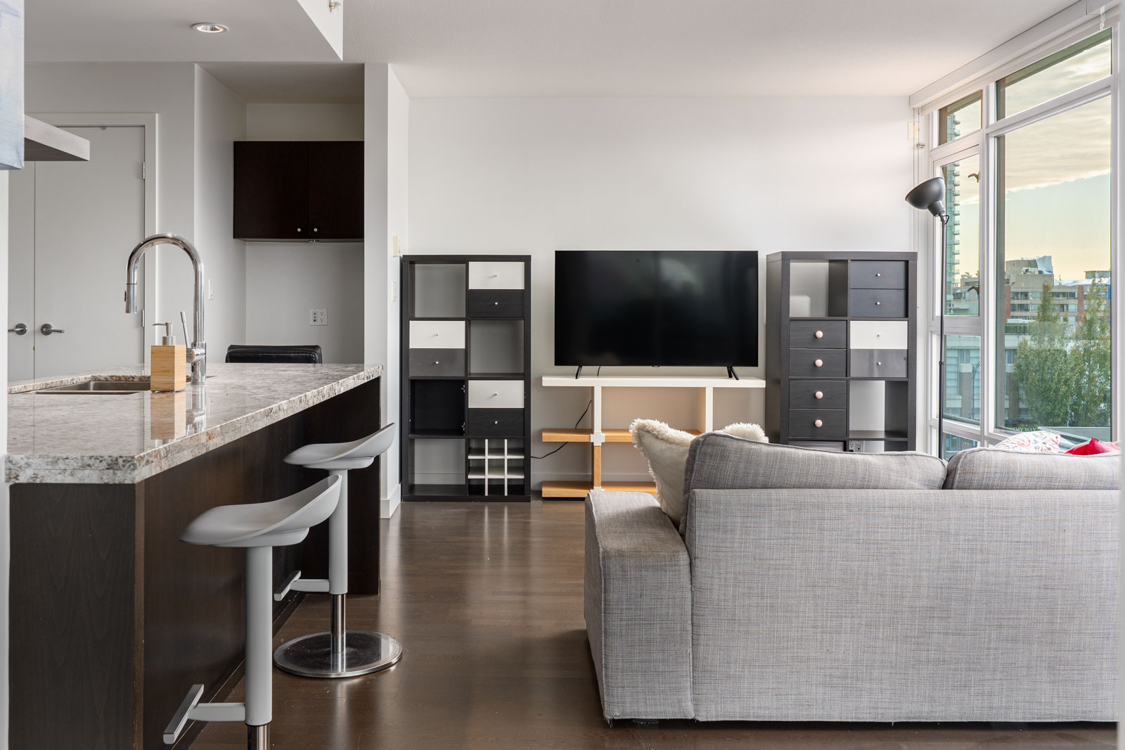 Modern living room and kitchen at 1455 George Street with a kitchen island, two stools, a sofa, and a wall-mounted TV.