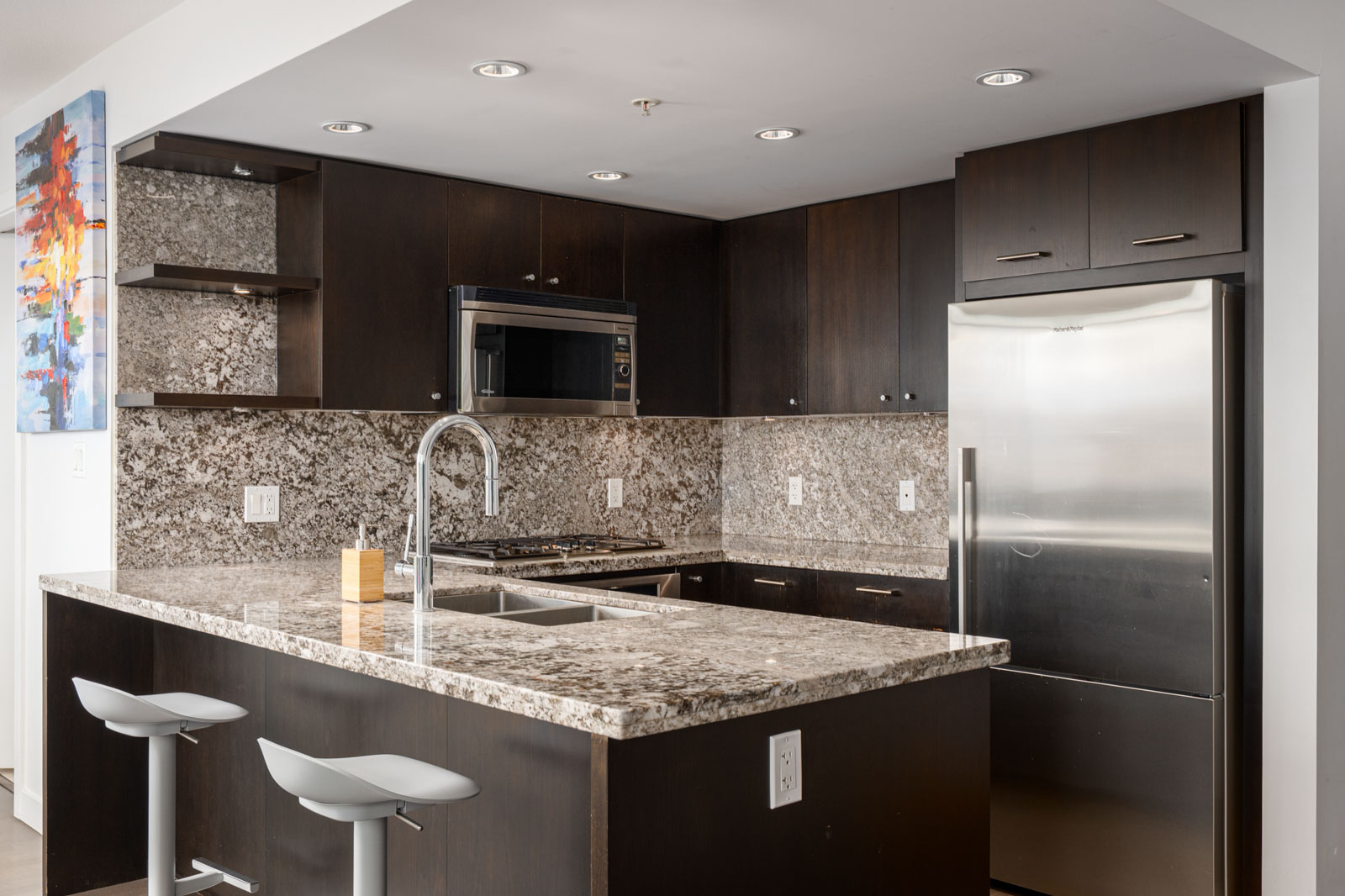 Modern kitchen at 1455 George Street with dark wood cabinets, granite countertops, stainless appliances, and two stools.