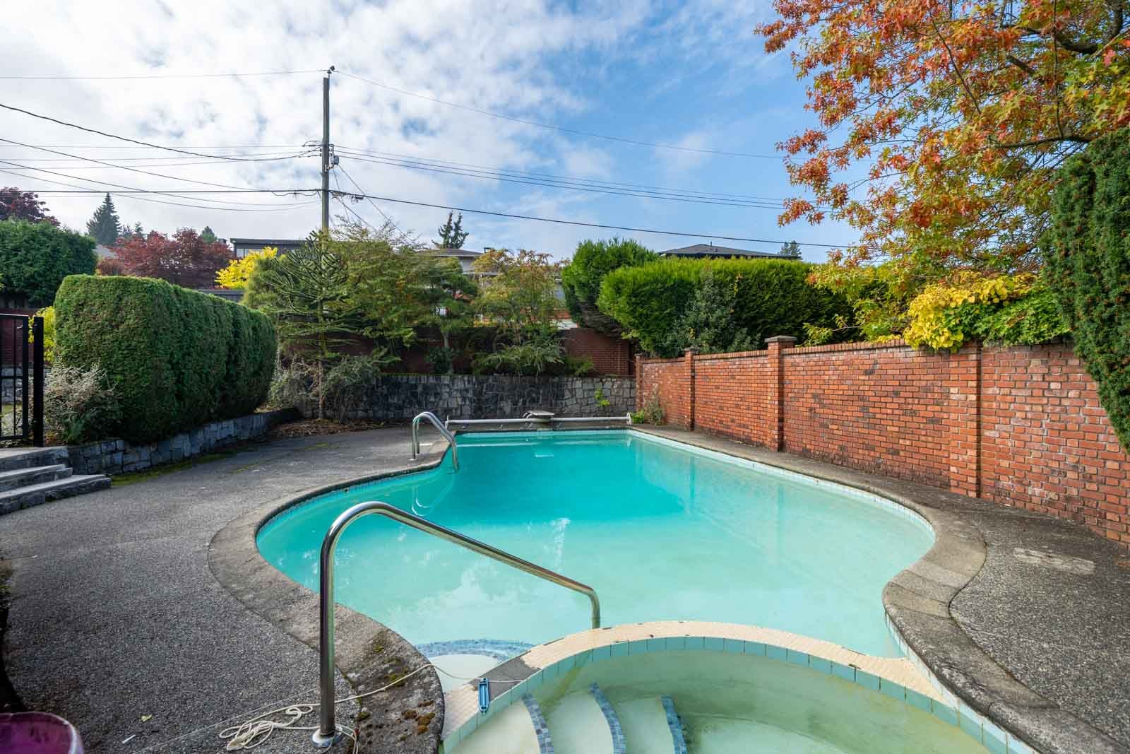 Outdoor pool and connected hot tub in a Vancouver basement-level backyard, framed by a brick wall and hedges.