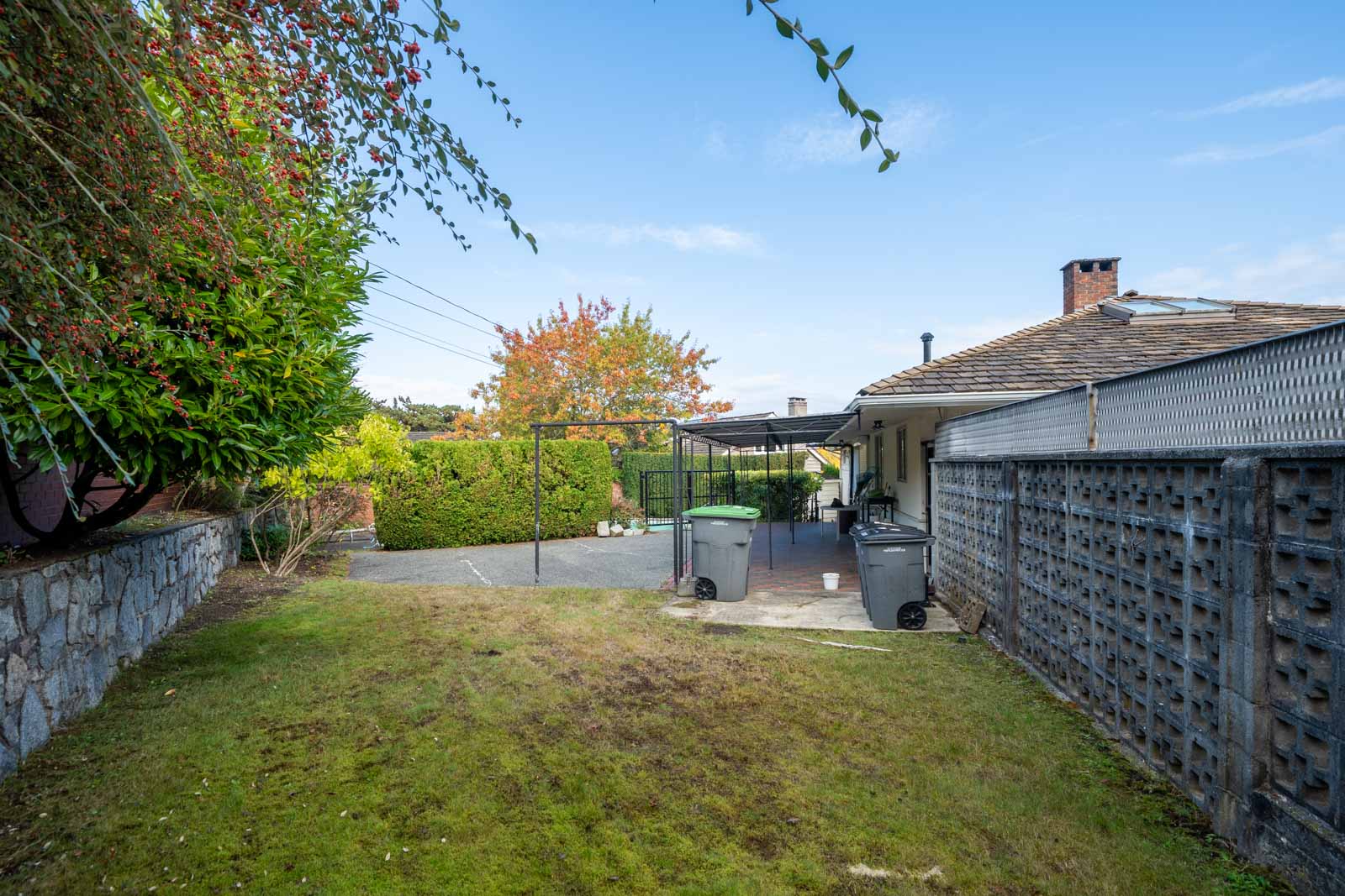 Vancouver basement backyard with a grassy lawn, paved patio, two garbage bins, and a side fence.